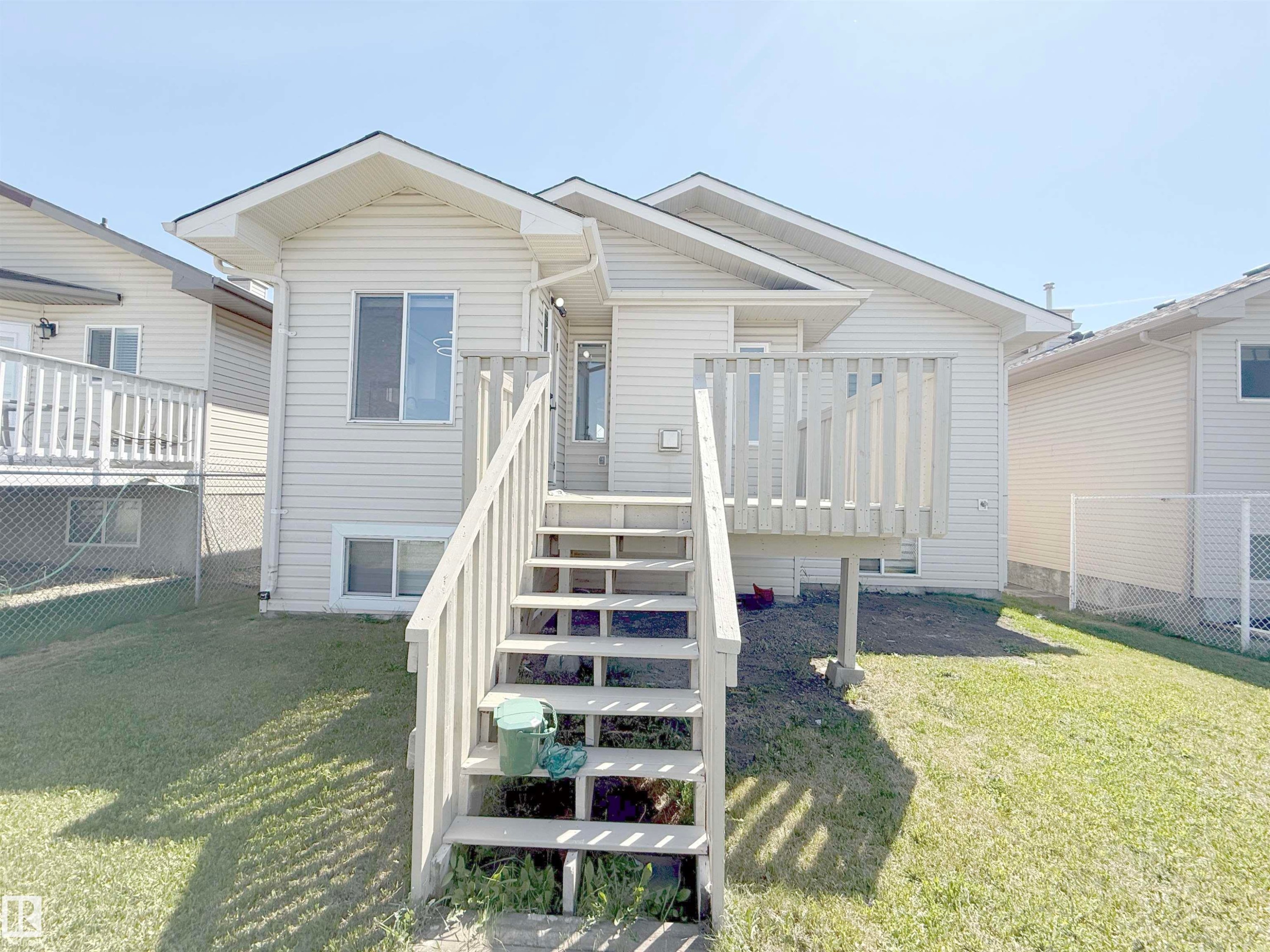 Rear exterior featuring light-toned horizontal siding, a wooden deck, and a full-height wooden staircase - 6144 166 Avenue, Edmonton, AB