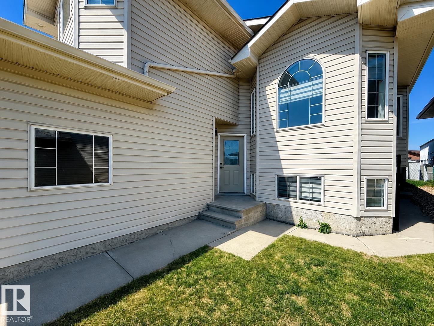 Exterior featuring light-toned horizontal siding, a prominent arched window, and a concrete pathway leading to the entry - 6144 166 Avenue, Edmonton, AB