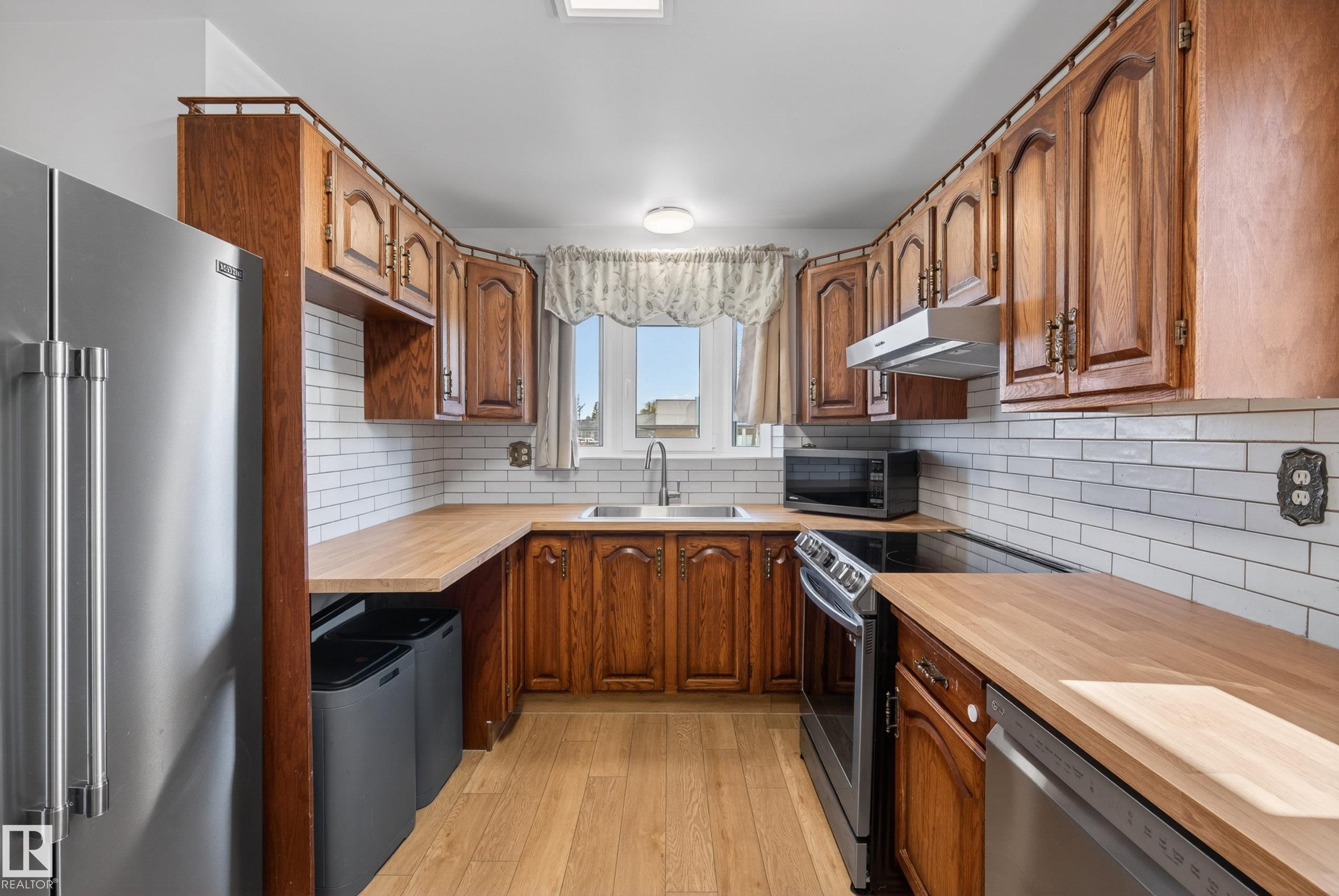 U-shaped kitchen featuring wood cabinetry, wood-finish countertops, and white subway tile backsplash - 6203 90 Avenue, Edmonton, AB