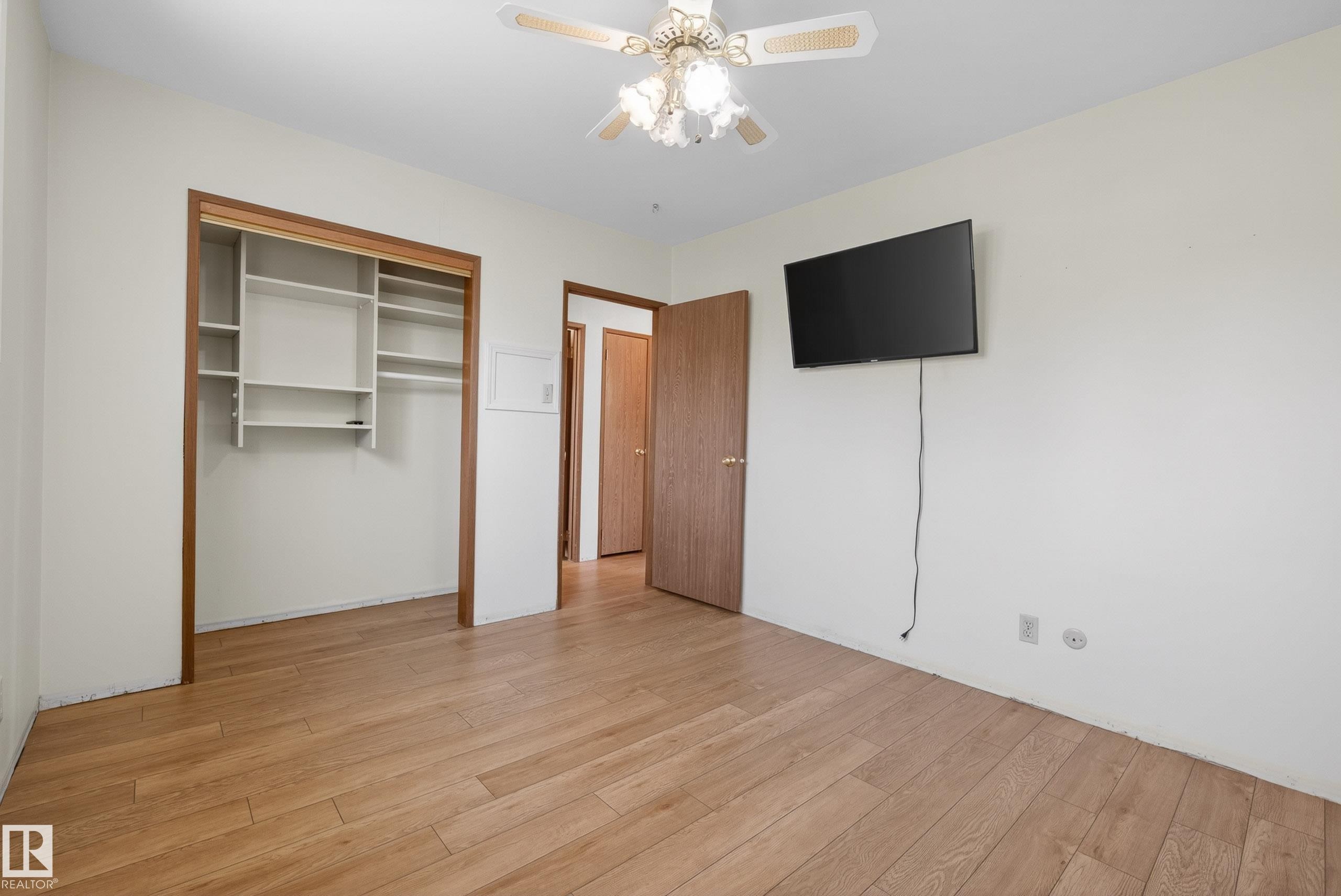 Room featuring wood-finish flooring, a built-in ceiling fan with light, and a closet with integrated shelving - 6203 90 Avenue, Edmonton, AB