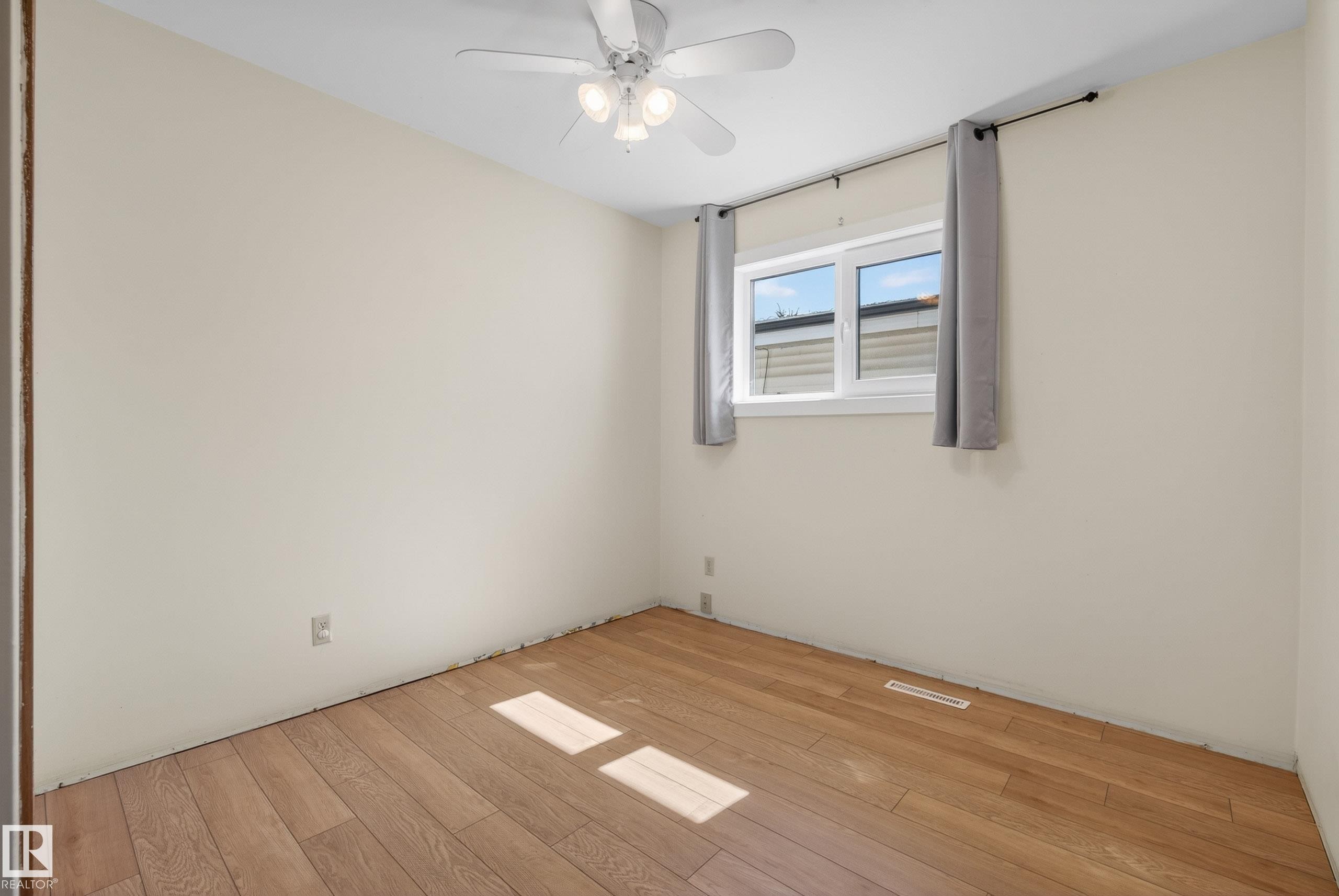 Neutral-toned room featuring wood-finish flooring and a ceiling fan with integrated lighting - 6203 90 Avenue, Edmonton, AB