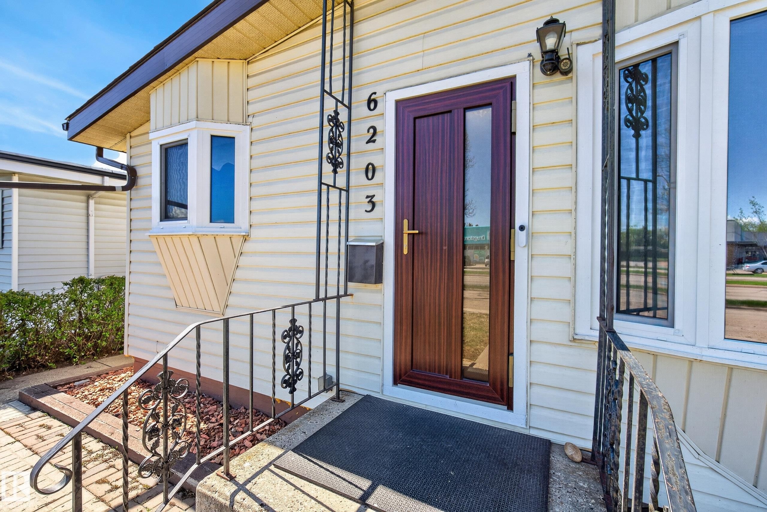 Front entrance featuring a dark wood-finish door with glass panels, white vinyl siding, and wrought iron railings - 6203 90 Avenue, Edmonton, AB