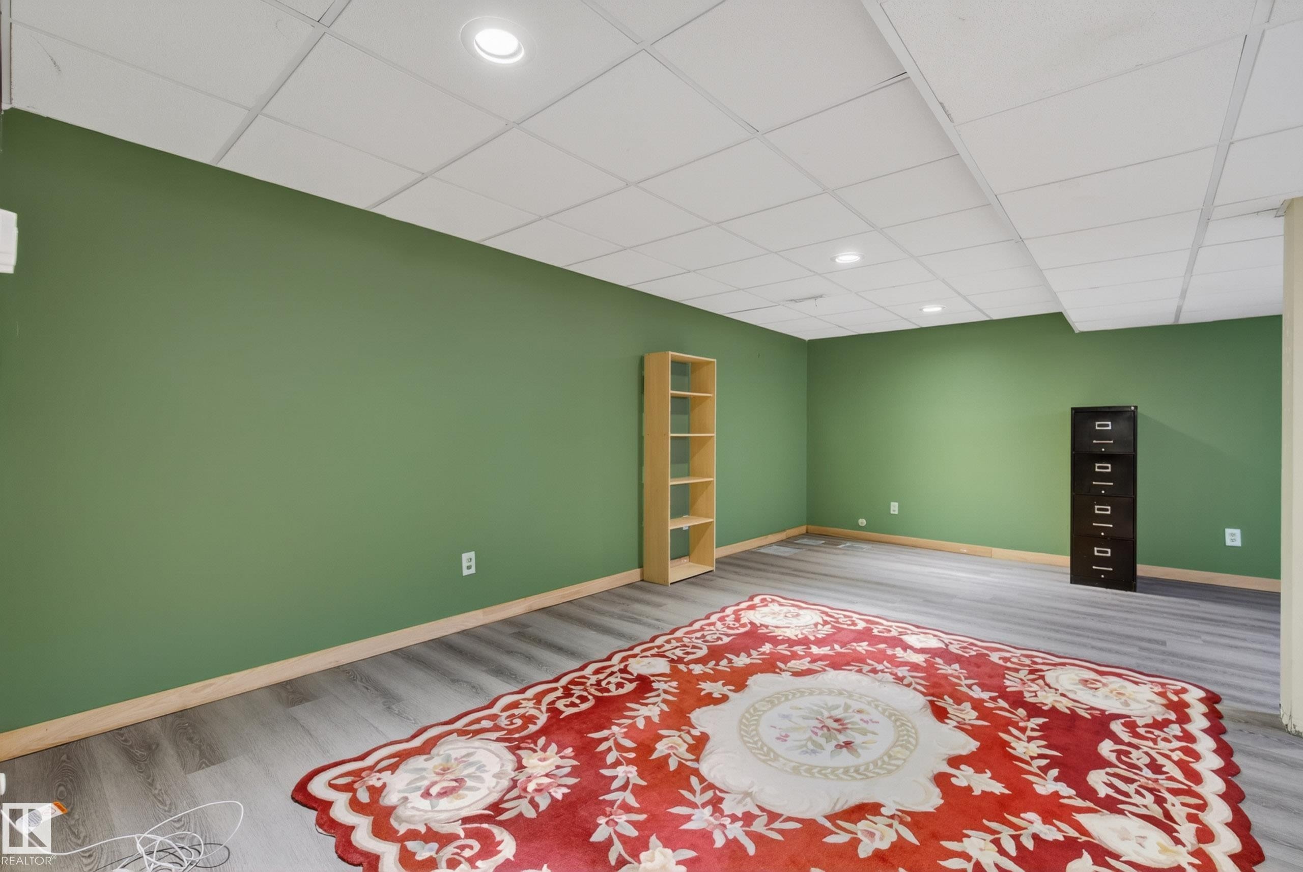 Spacious room featuring green walls, wood-finish flooring, and a drop ceiling with recessed lighting - 6203 90 Avenue, Edmonton, AB