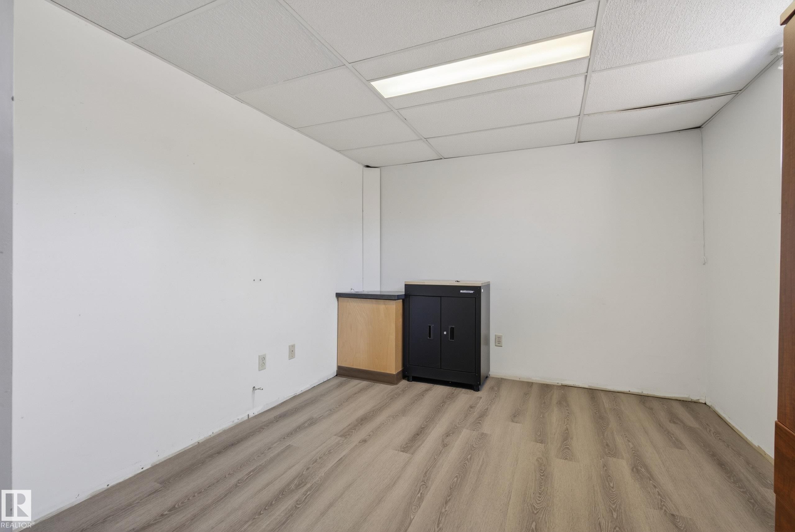 Spacious interior room featuring wood-finish flooring, white walls, and a dropped ceiling with integrated lighting - 6203 90 Avenue, Edmonton, AB