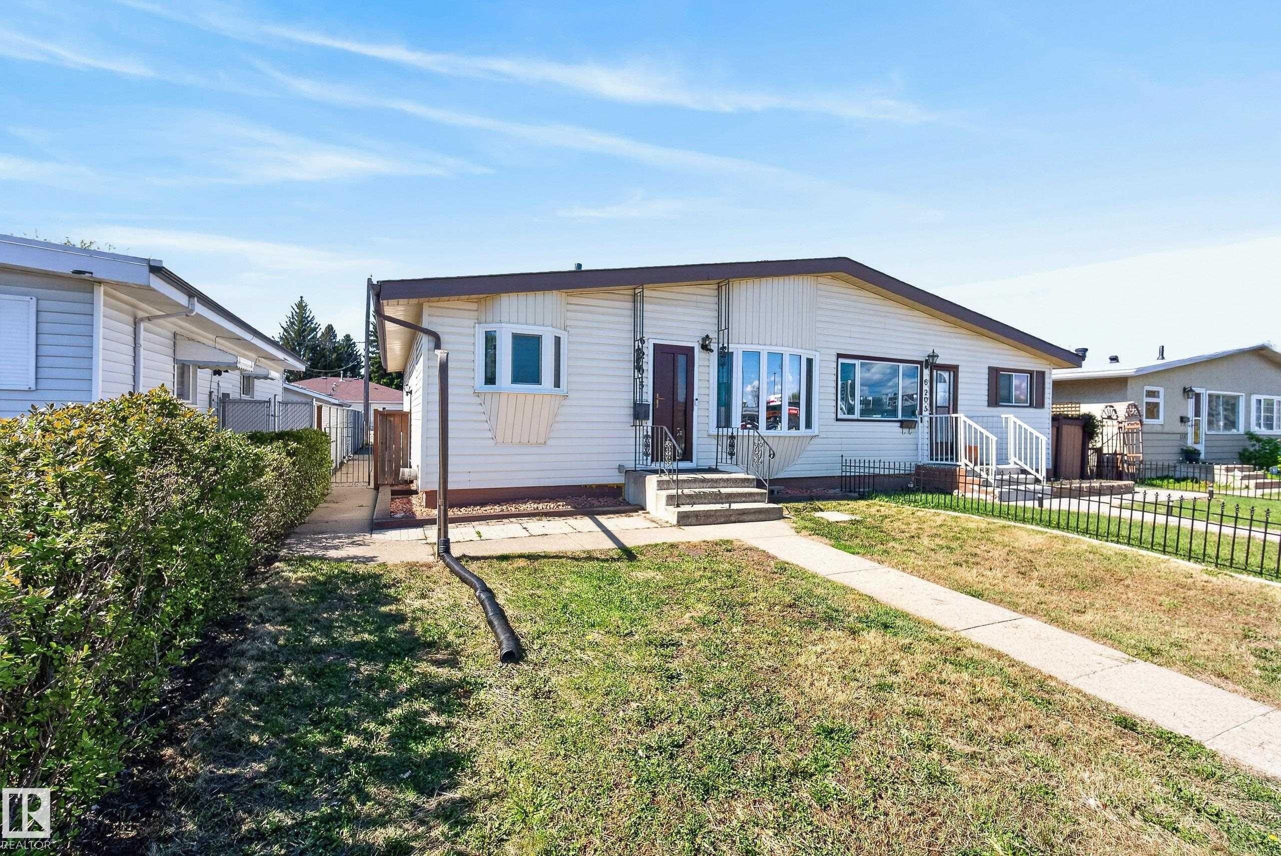 Single-story residence featuring light-colored siding, a brown trim roofline, and a prominent bay window - 6203 90 Avenue, Edmonton, AB