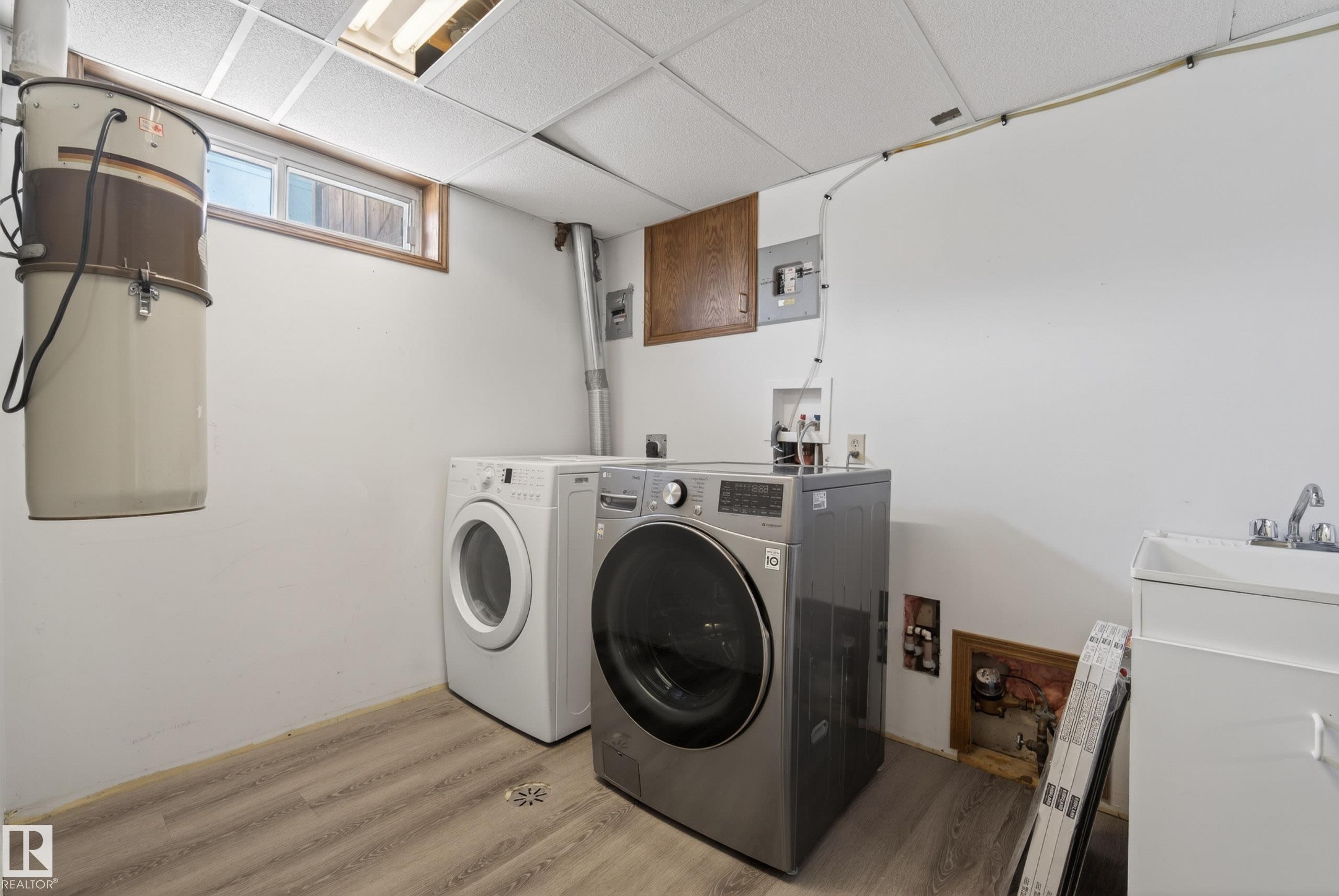Laundry area featuring wood-finish flooring, a utility sink with a chrome faucet, a drop-ceiling with recessed lighting, and a built-in central vacuum system - 6203 90 Avenue, Edmonton, AB