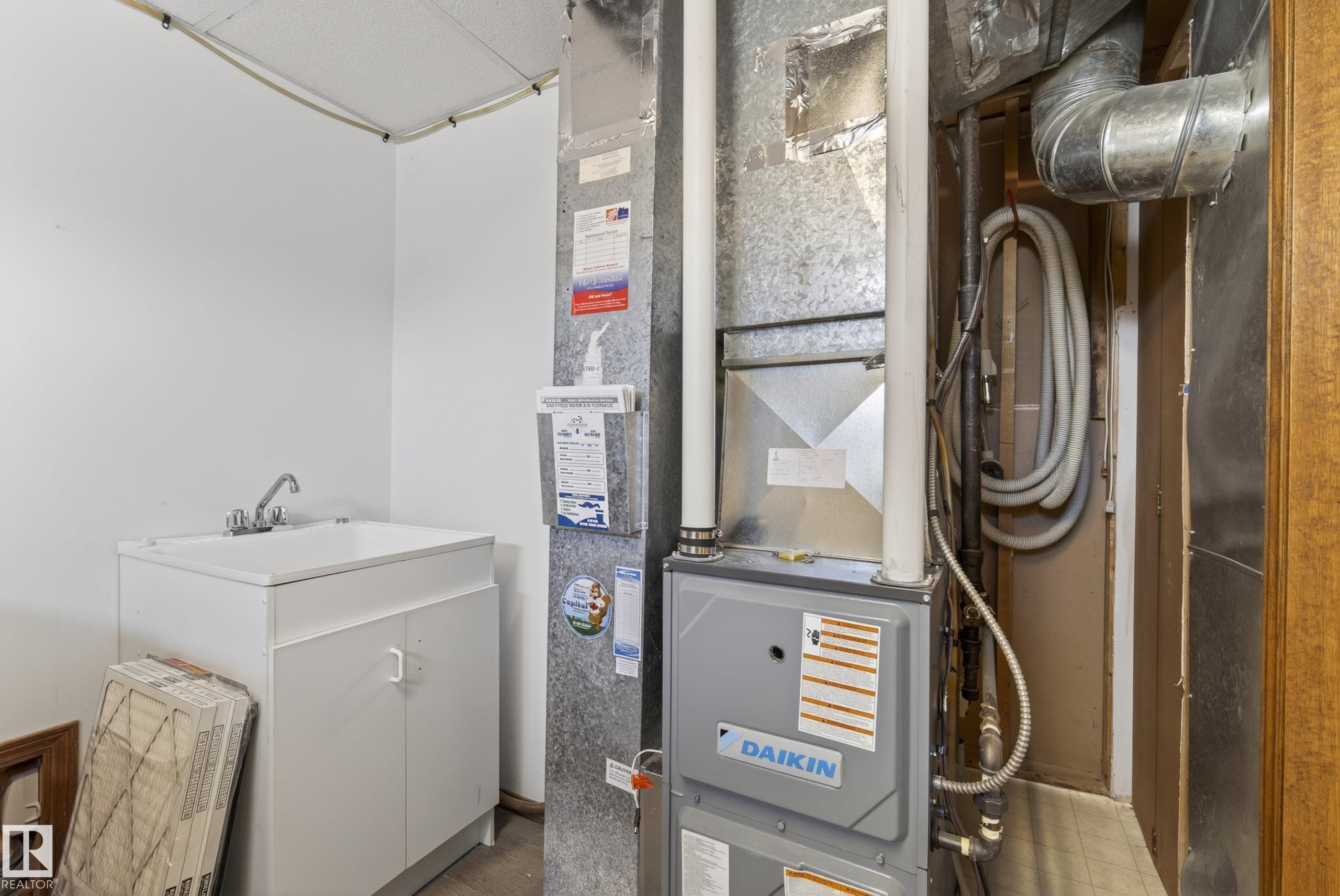 Utility area featuring a white utility sink with a chrome faucet, white base cabinetry, and a Daikin HVAC system with exposed ductwork - 6203 90 Avenue, Edmonton, AB