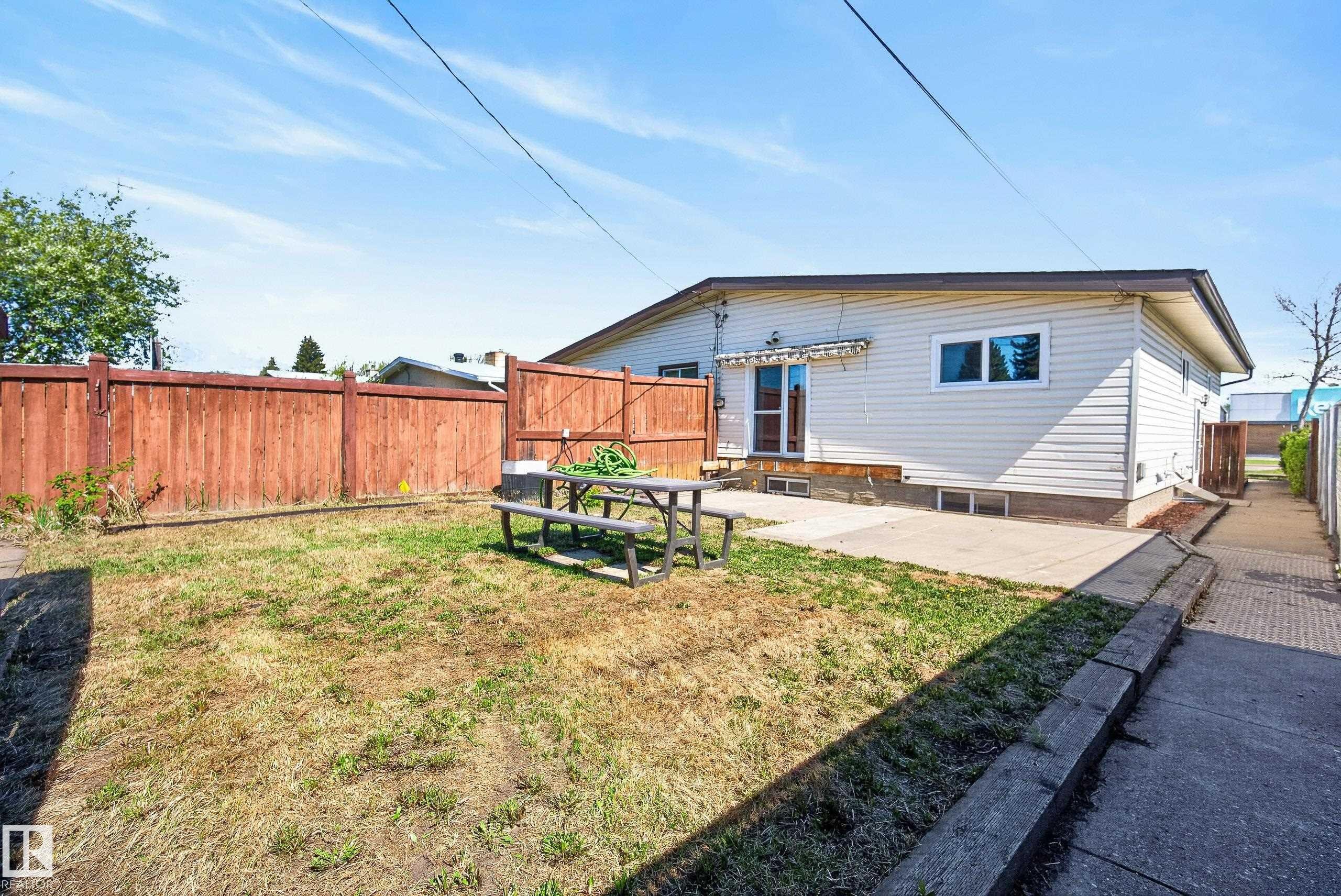 Fenced backyard featuring a concrete patio, a wood deck, and an exterior door with an awning - 6203 90 Avenue, Edmonton, AB