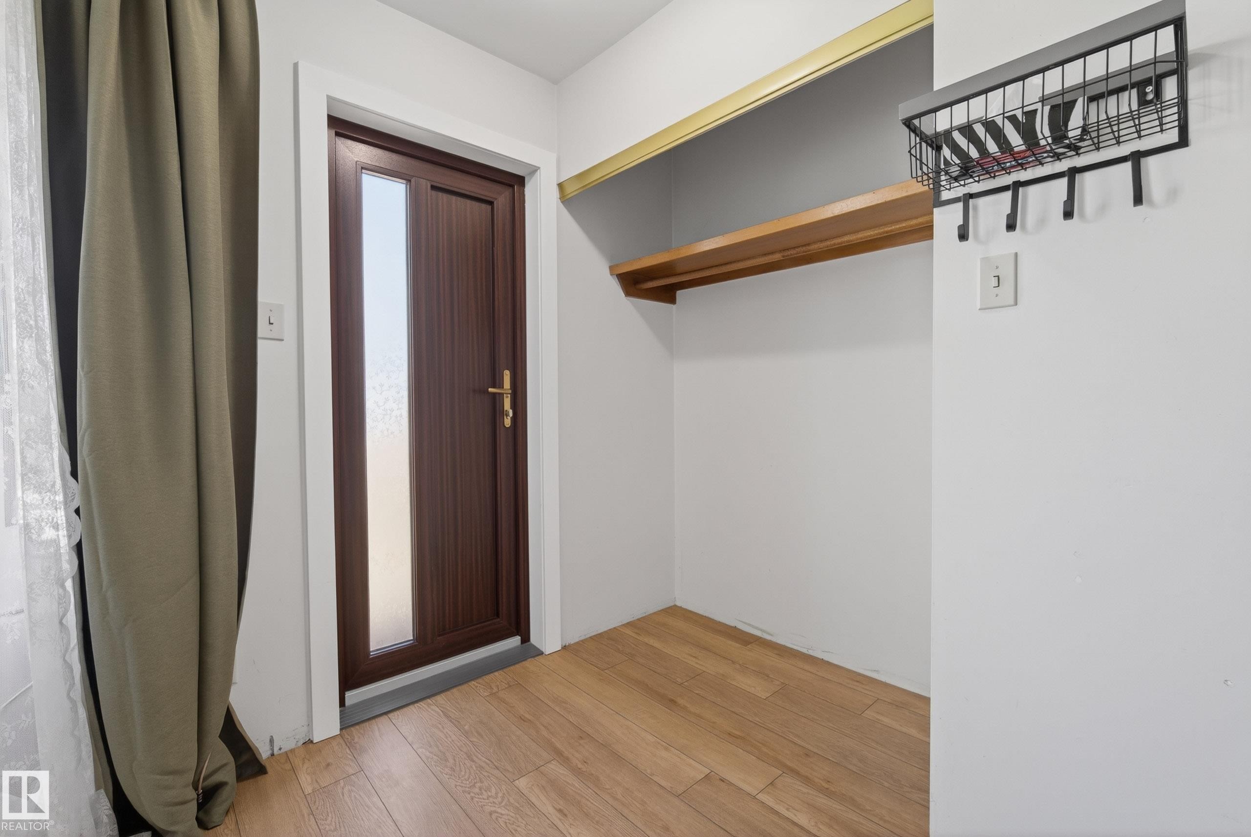 Entryway featuring wood-finish flooring, a wood-panel door with privacy glass, white trim, and a built-in storage shelf with a hanging rod - 6203 90 Avenue, Edmonton, AB