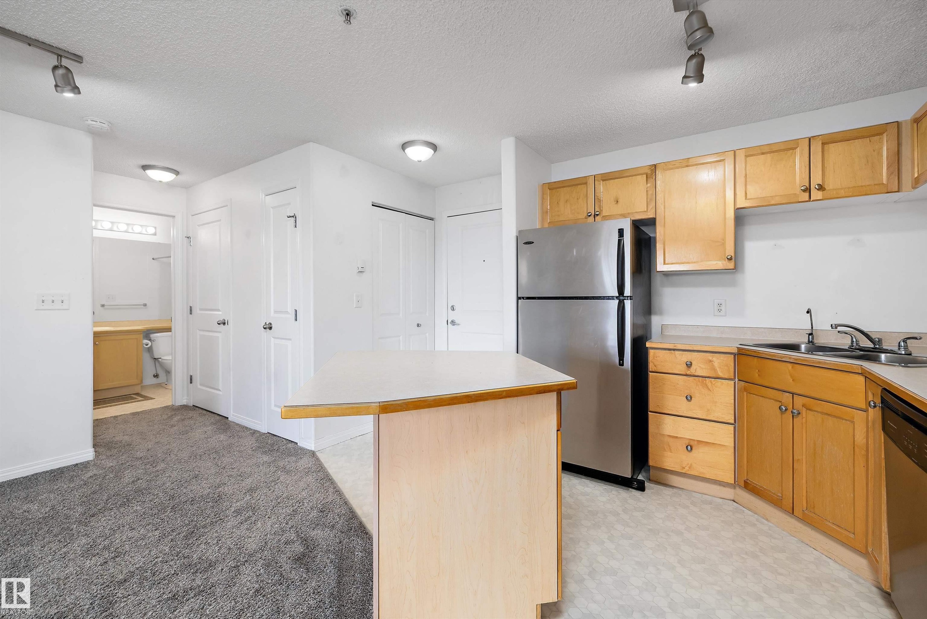 Kitchen with wood-finish cabinetry, stainless steel refrigerator, and integrated sink - 320 245 Edwards Drive, Edmonton, AB