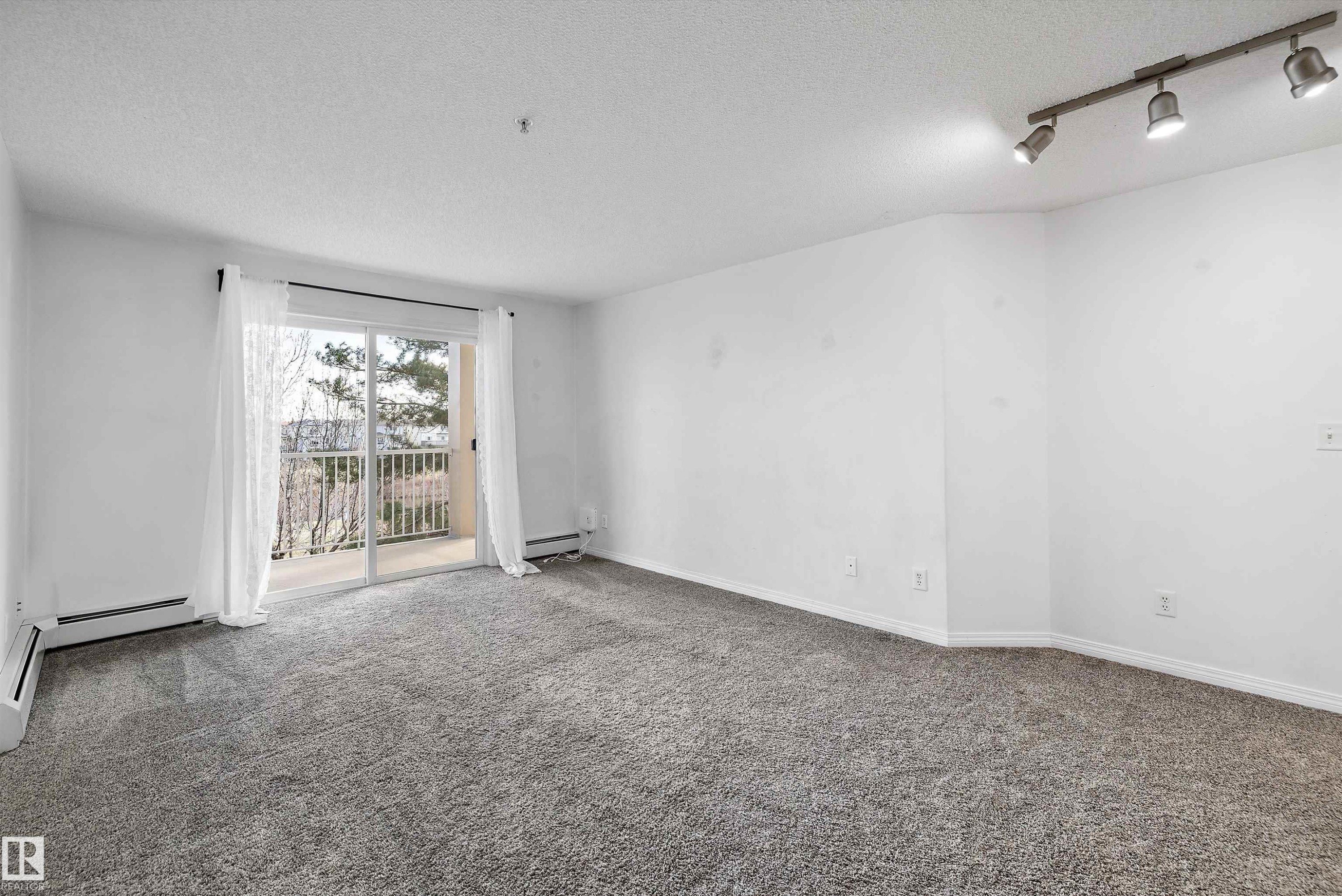 Spacious room featuring neutral carpeting, white walls, and a sliding glass door leading to a balcony - 320 245 Edwards Drive, Edmonton, AB