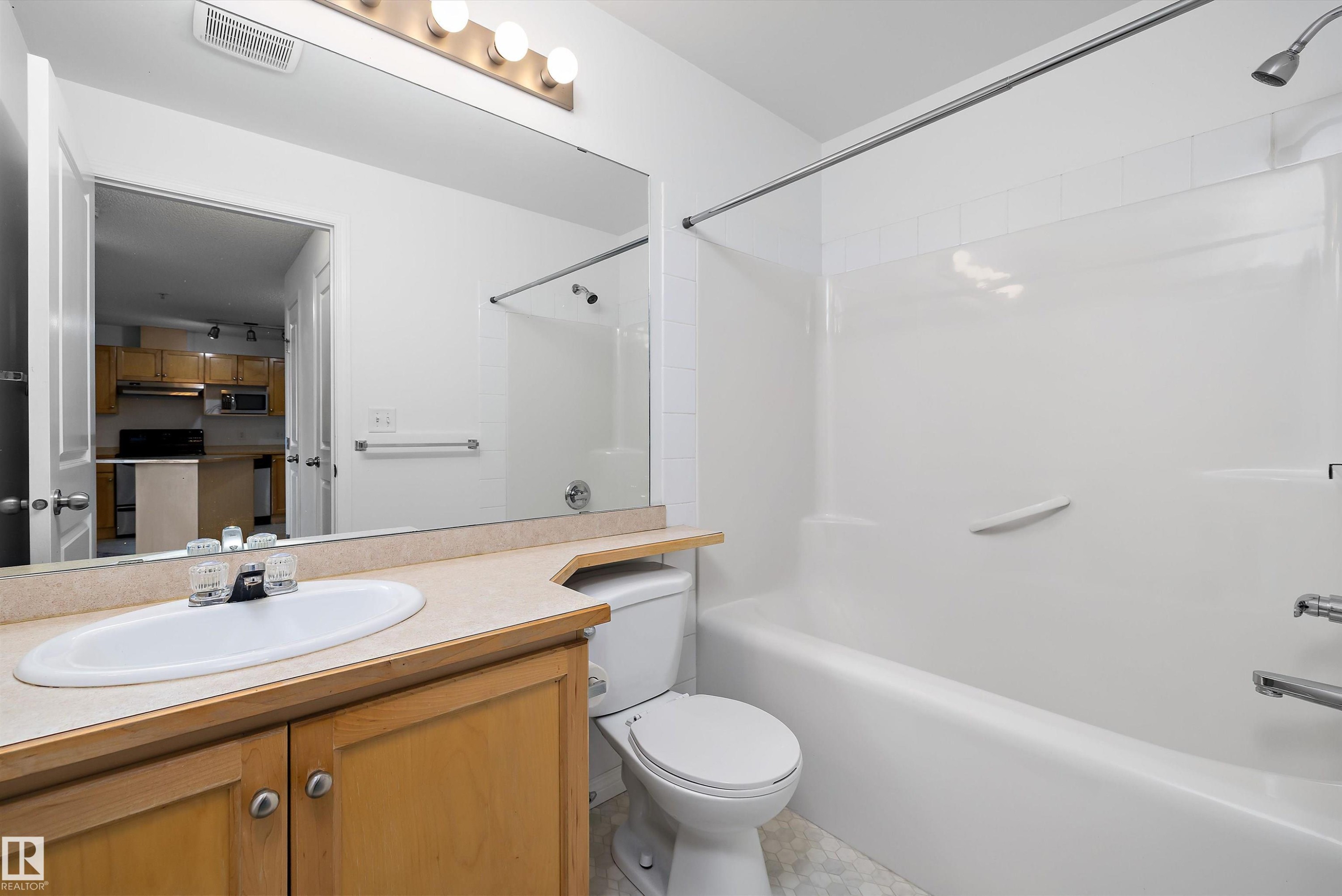 Bathroom featuring a light wood-finish vanity with a single basin sink, integrated countertop, and a full-width mirror - 320 245 Edwards Drive, Edmonton, AB