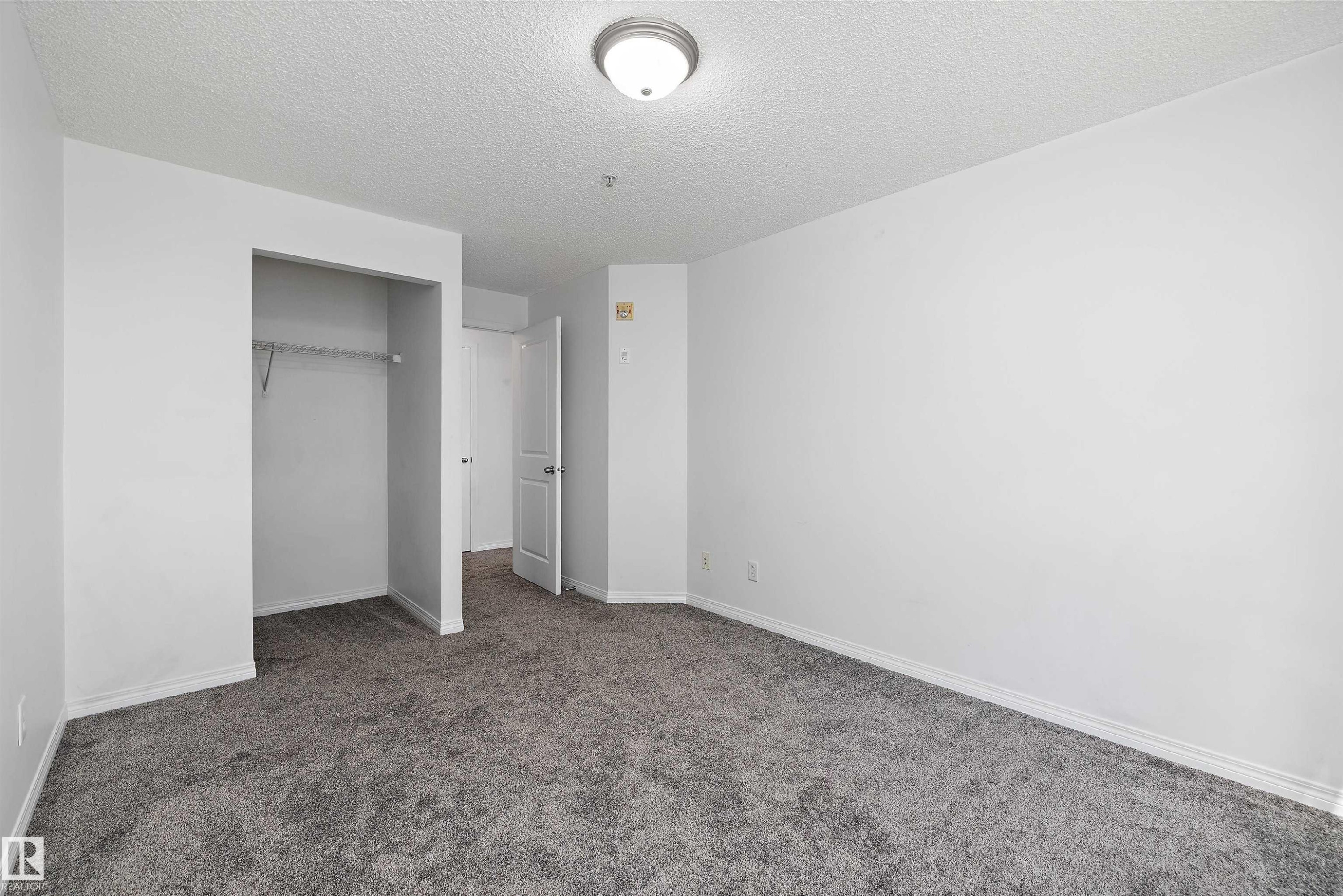 Spacious room featuring neutral grey carpeting, white walls, and a built-in closet with shelving - 320 245 Edwards Drive, Edmonton, AB