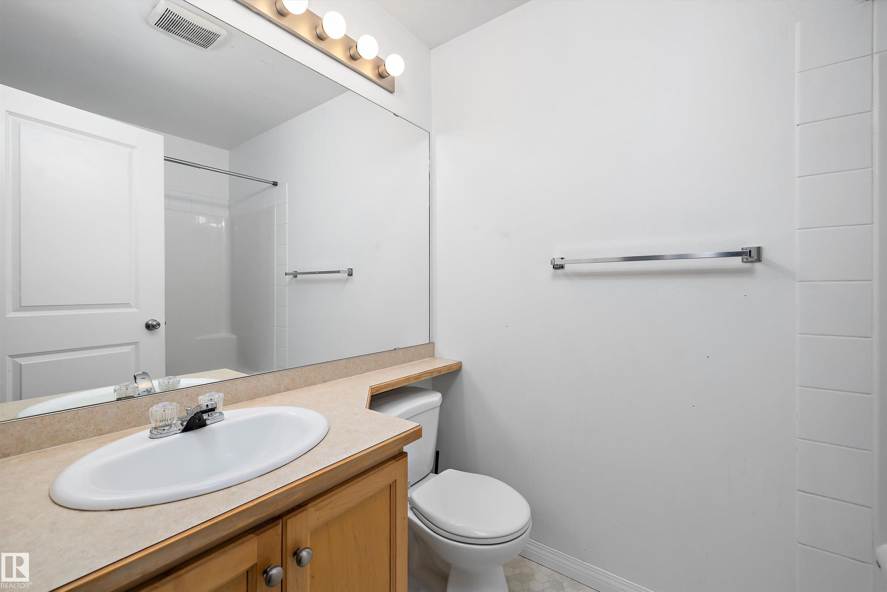 Bathroom featuring a wood vanity with a solid surface countertop, an oval undermount sink, and a mirrored wall with an overhead vanity light fixture - 320 245 Edwards Drive, Edmonton, AB