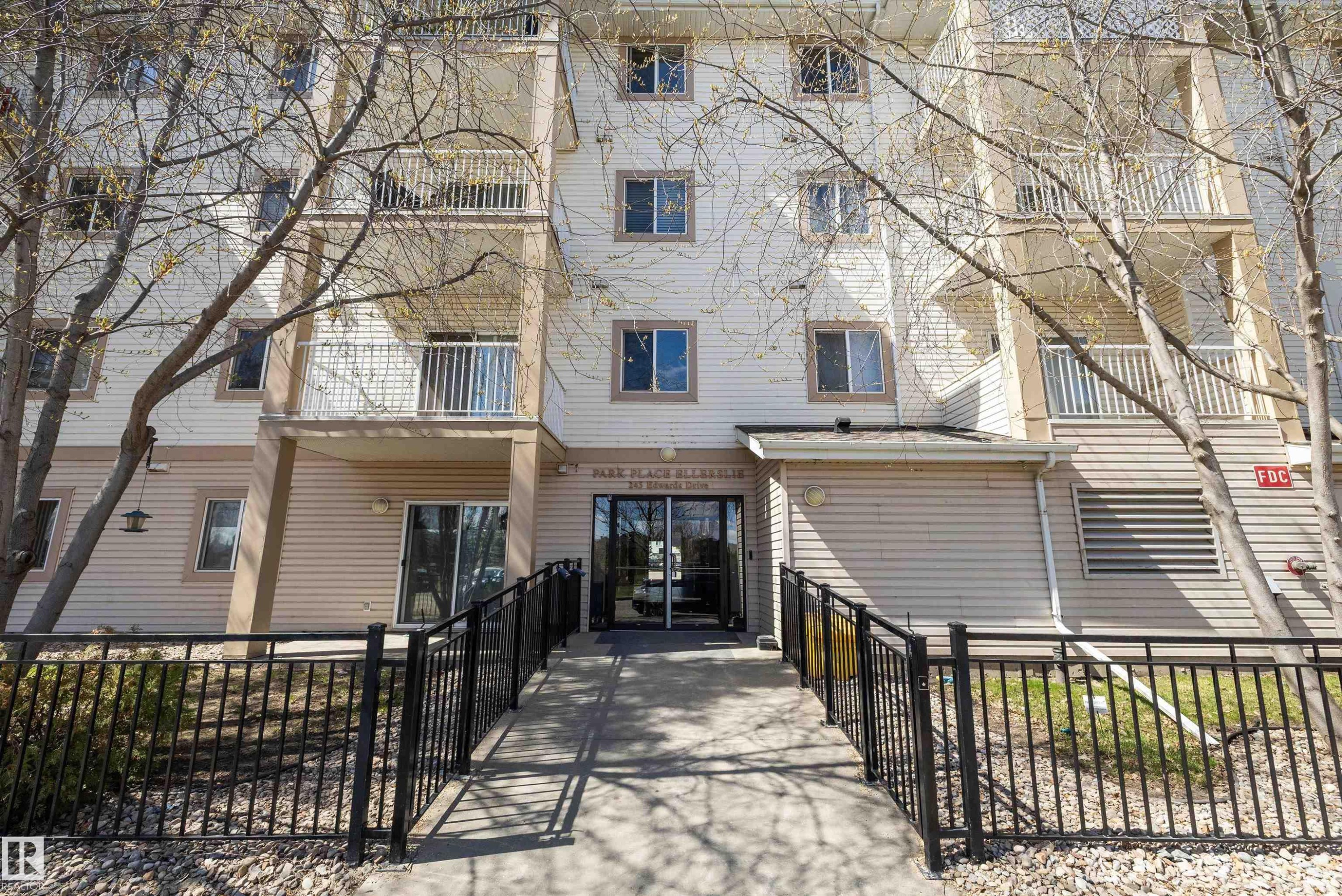 Multi-story building featuring light-colored siding, multiple balconies with white railings, and a ground-level entrance - 320 245 Edwards Drive, Edmonton, AB