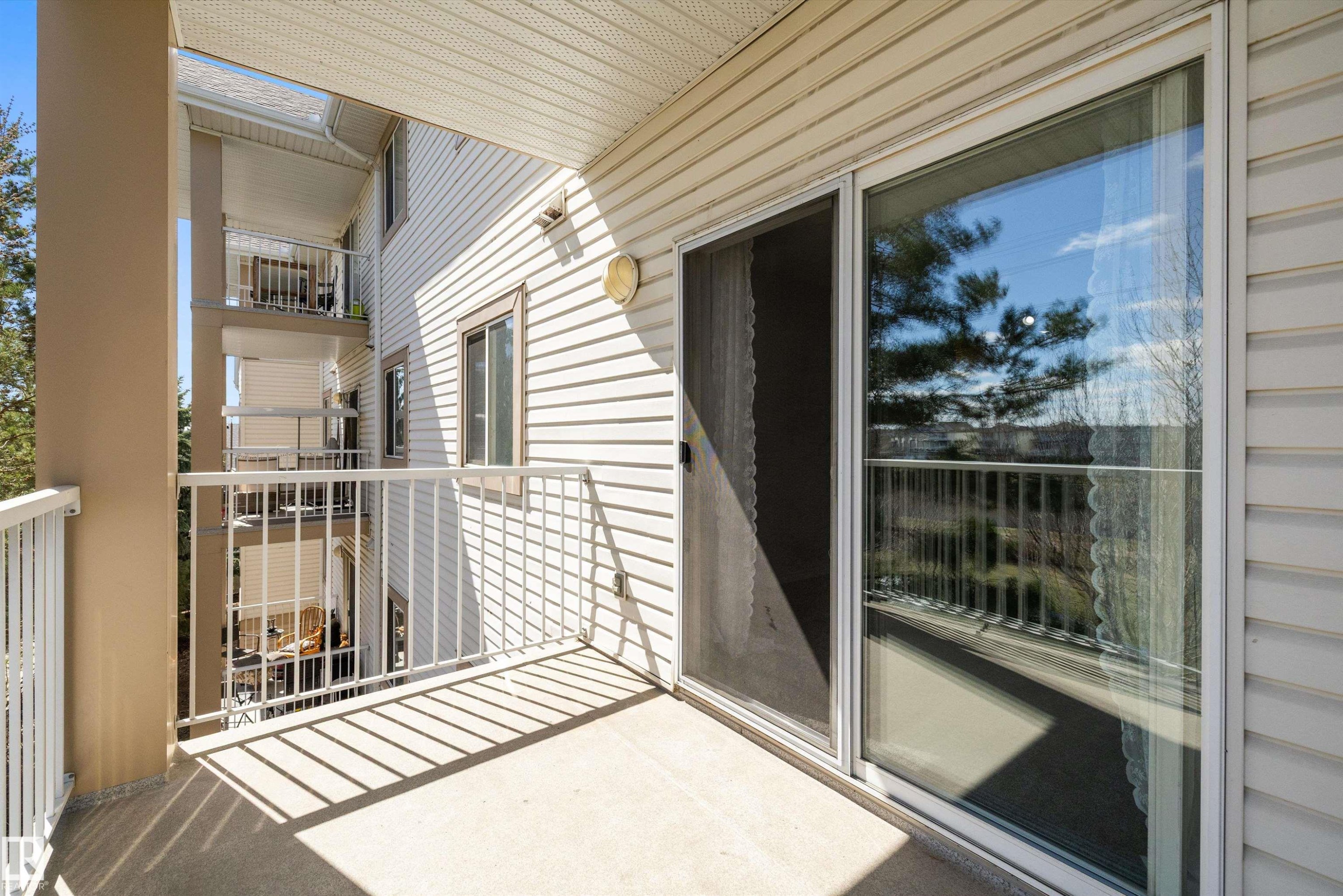Private balcony with concrete flooring and white metal railings, featuring a sliding glass door and an exterior wall light fixture - 320 245 Edwards Drive, Edmonton, AB