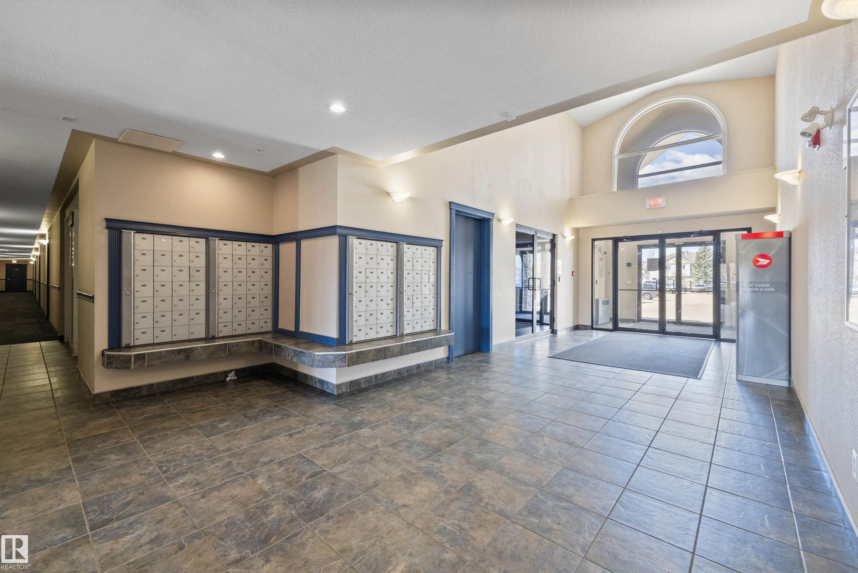 Spacious lobby featuring large format tile flooring, a high vaulted ceiling with an arched window, and recessed lighting - 320 245 Edwards Drive, Edmonton, AB