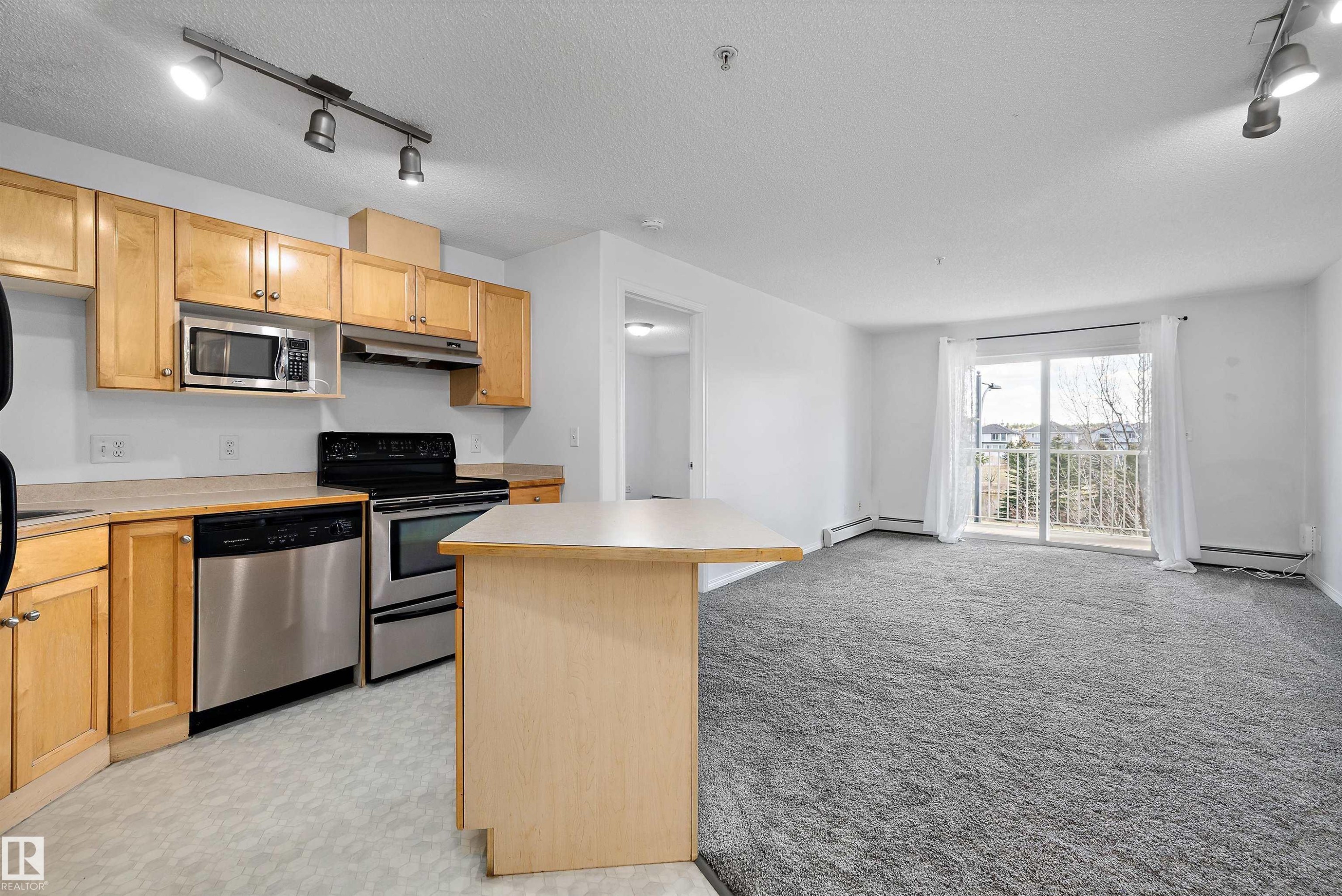 Open-concept living area with a kitchen featuring natural wood cabinetry, stainless steel appliances, and a central island - 320 245 Edwards Drive, Edmonton, AB