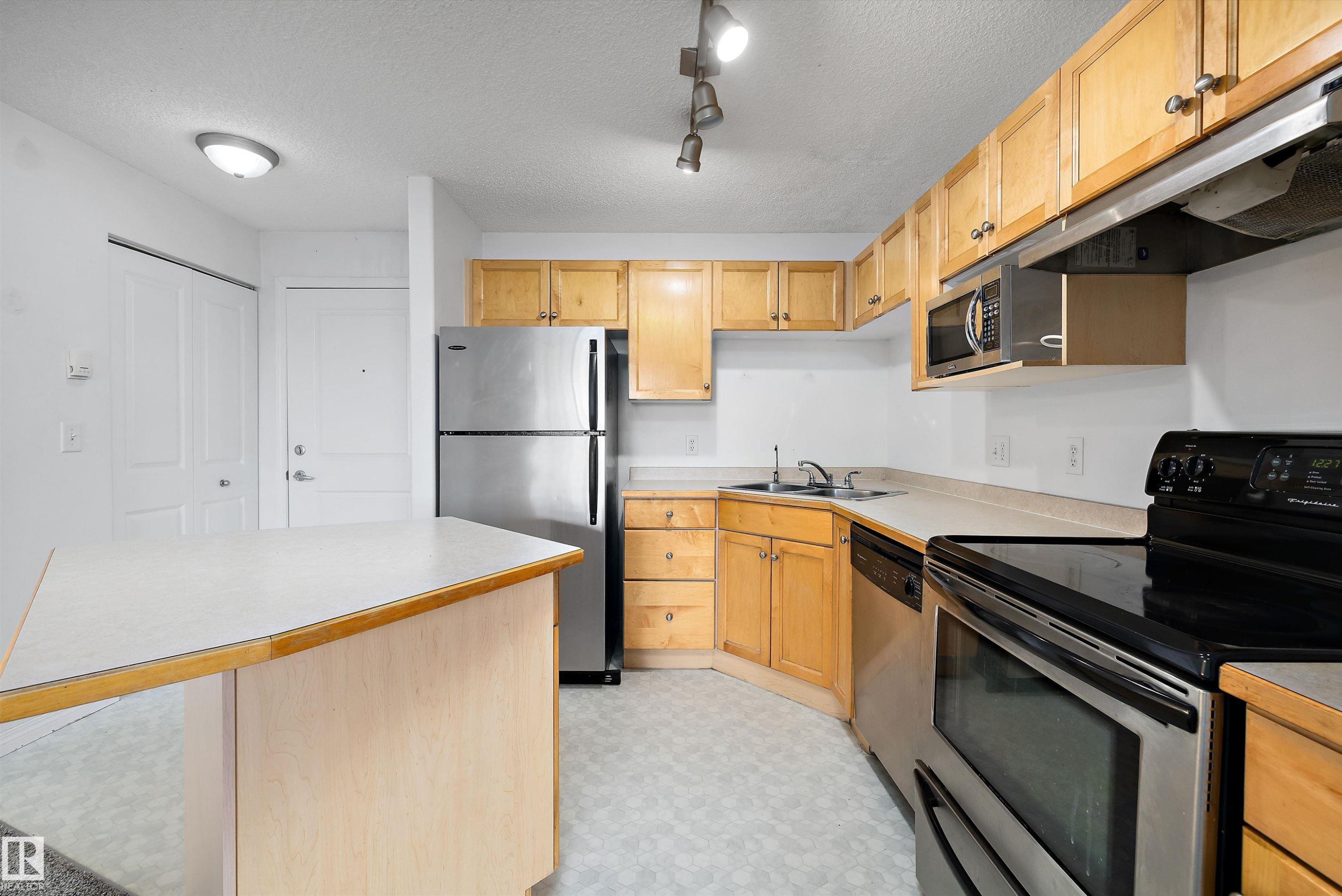 Kitchen featuring wood cabinetry, stainless steel appliances, a corner sink, a built-in microwave, and track lighting - 320 245 Edwards Drive, Edmonton, AB
