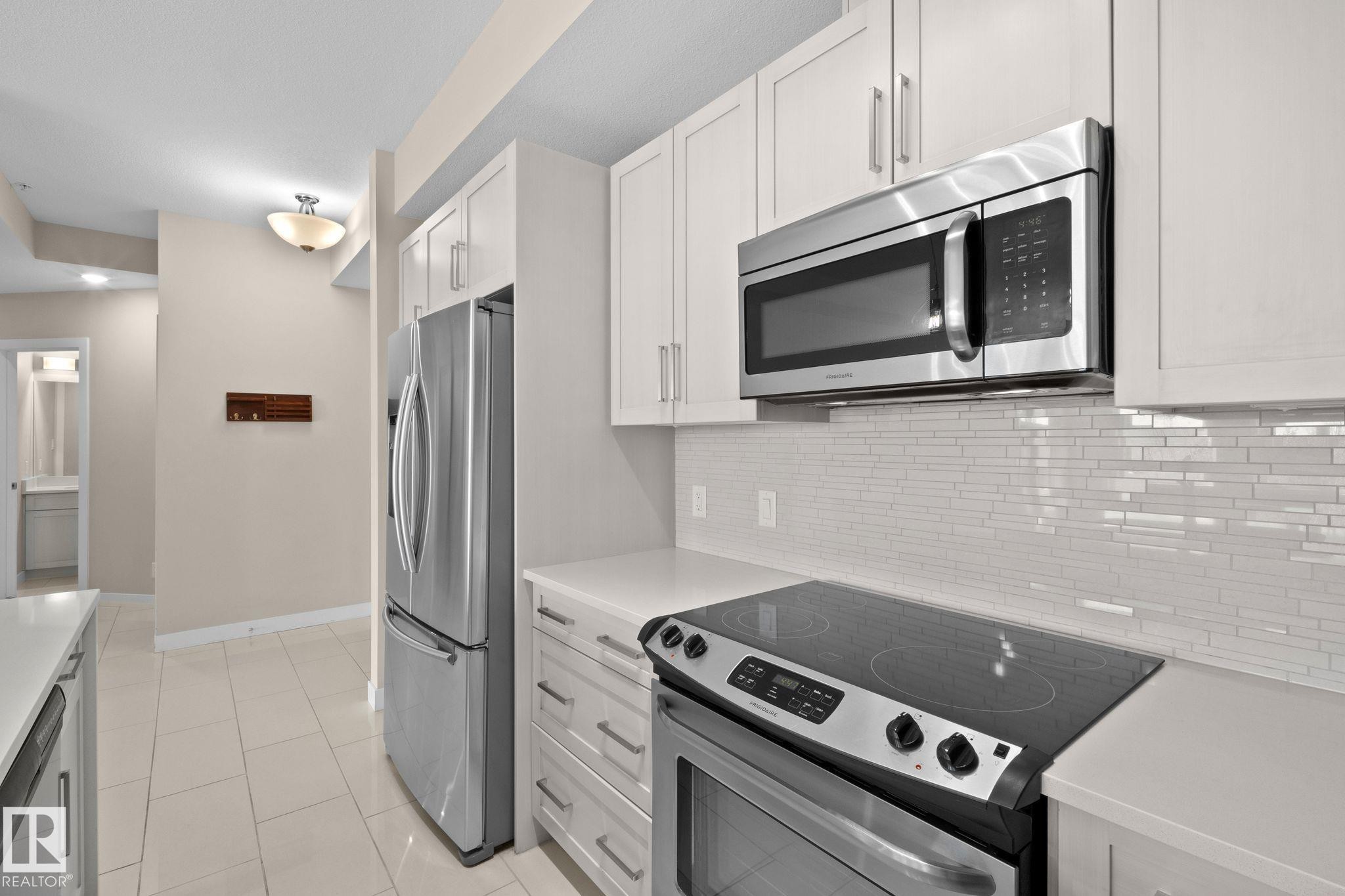 Modern kitchen featuring white shaker cabinetry, stainless steel appliances, a smooth-top range, white countertops, and a white subway tile backsplash - 309 625 Leger Way, Edmonton, AB