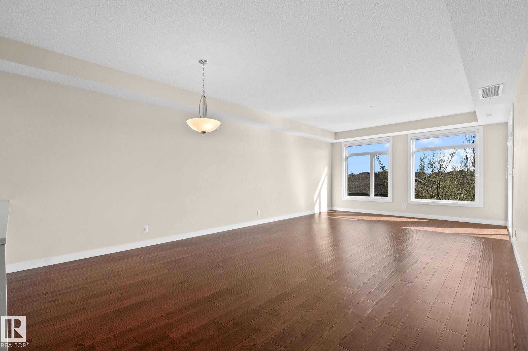 Spacious interior featuring wood-finish flooring, neutral-toned walls, and white trim - 309 625 Leger Way, Edmonton, AB