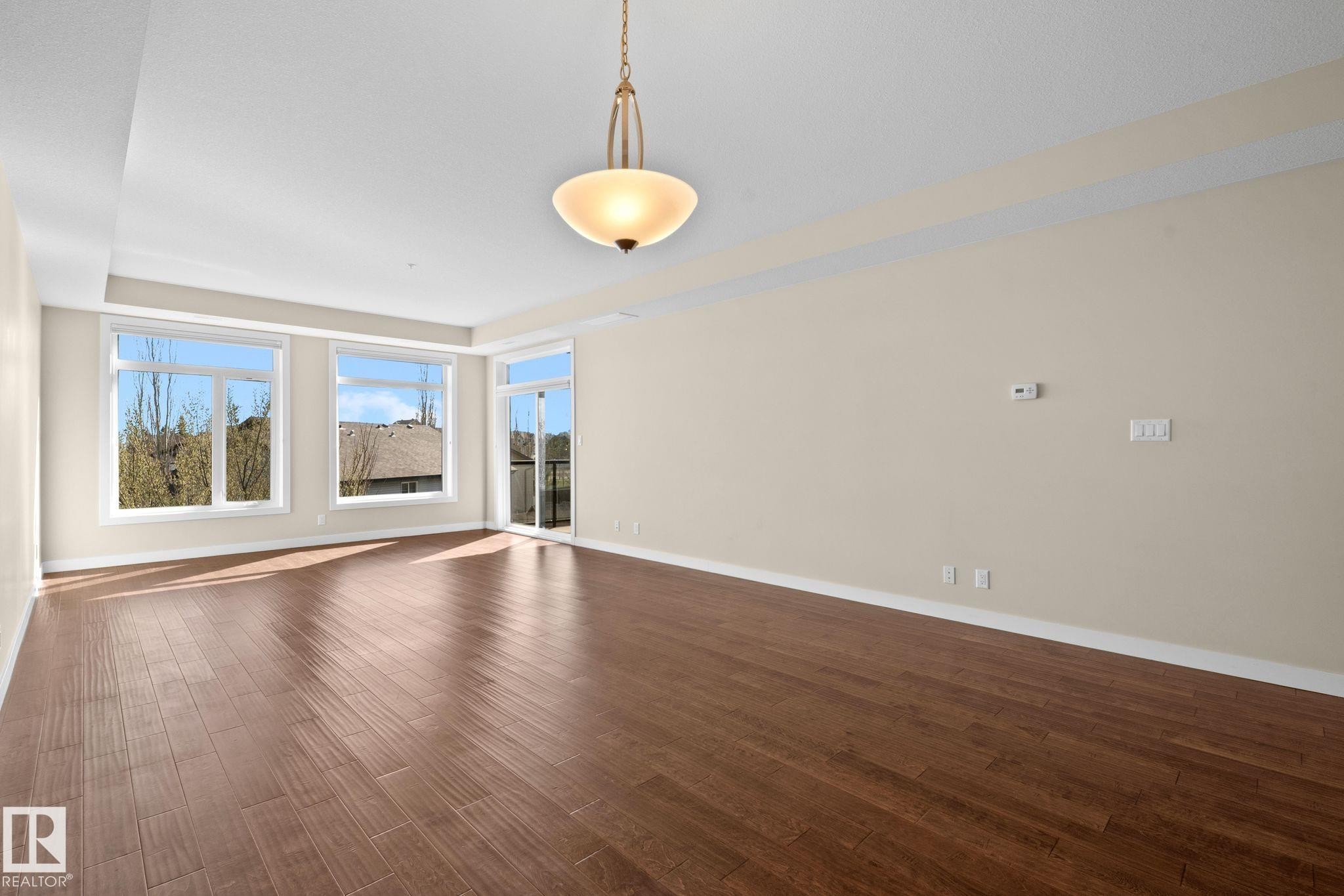 Spacious room featuring wood-finish flooring, light neutral wall tones, and recessed ceiling details - 309 625 Leger Way, Edmonton, AB
