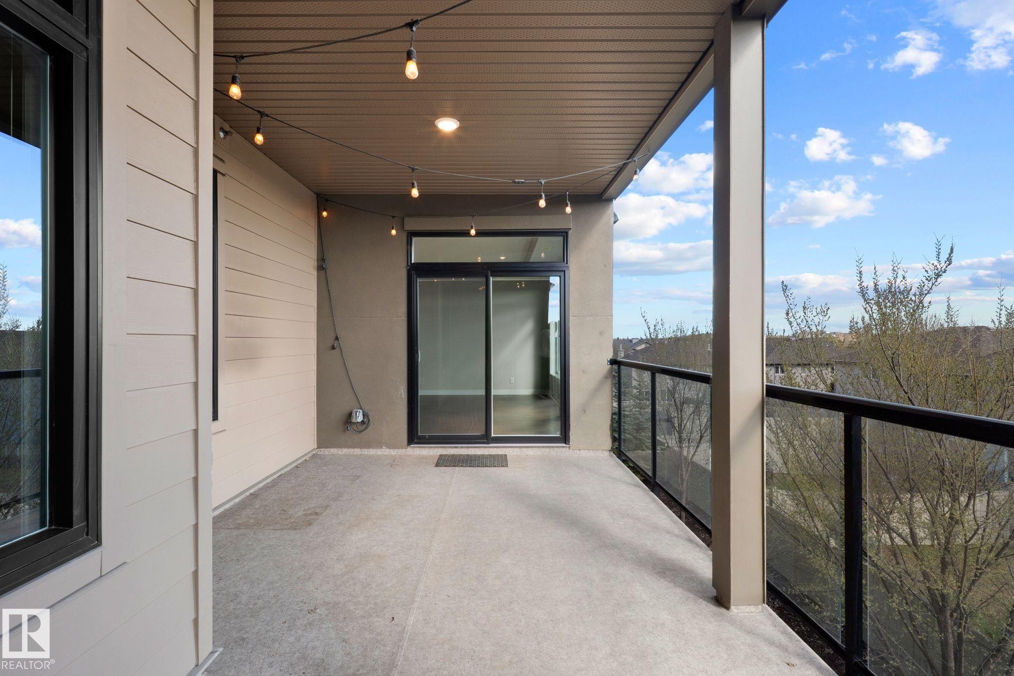 Spacious private balcony with concrete flooring, glass panel railing, and string lighting - 309 625 Leger Way, Edmonton, AB