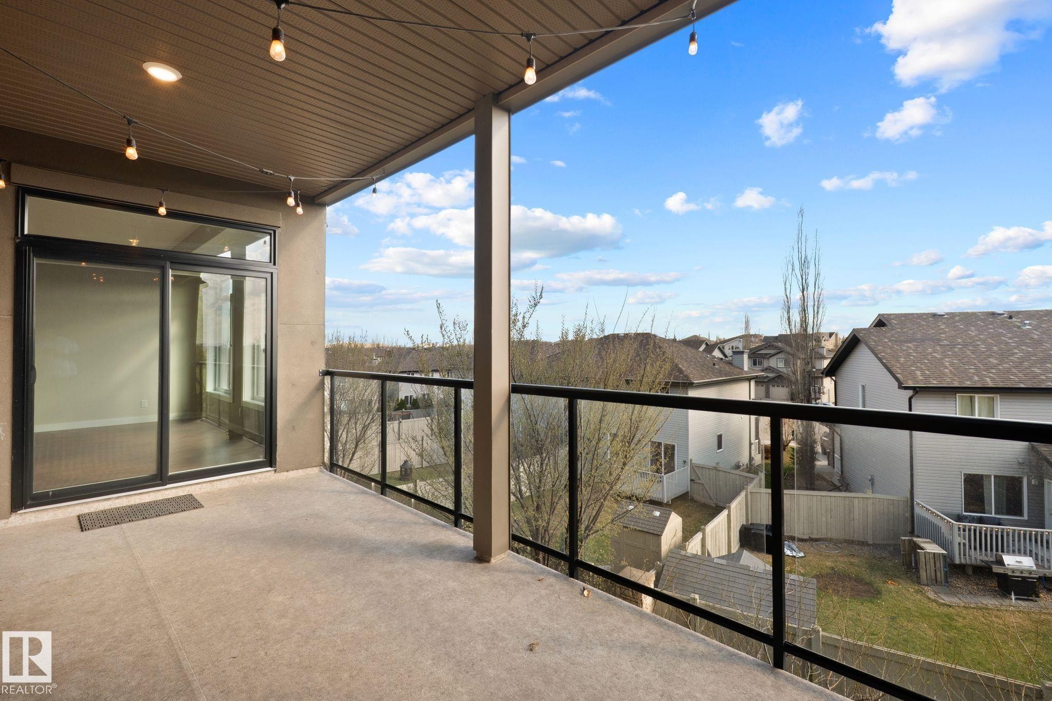 Private concrete balcony featuring a glass railing, black aluminum frame, and a sliding glass patio door - 309 625 Leger Way, Edmonton, AB