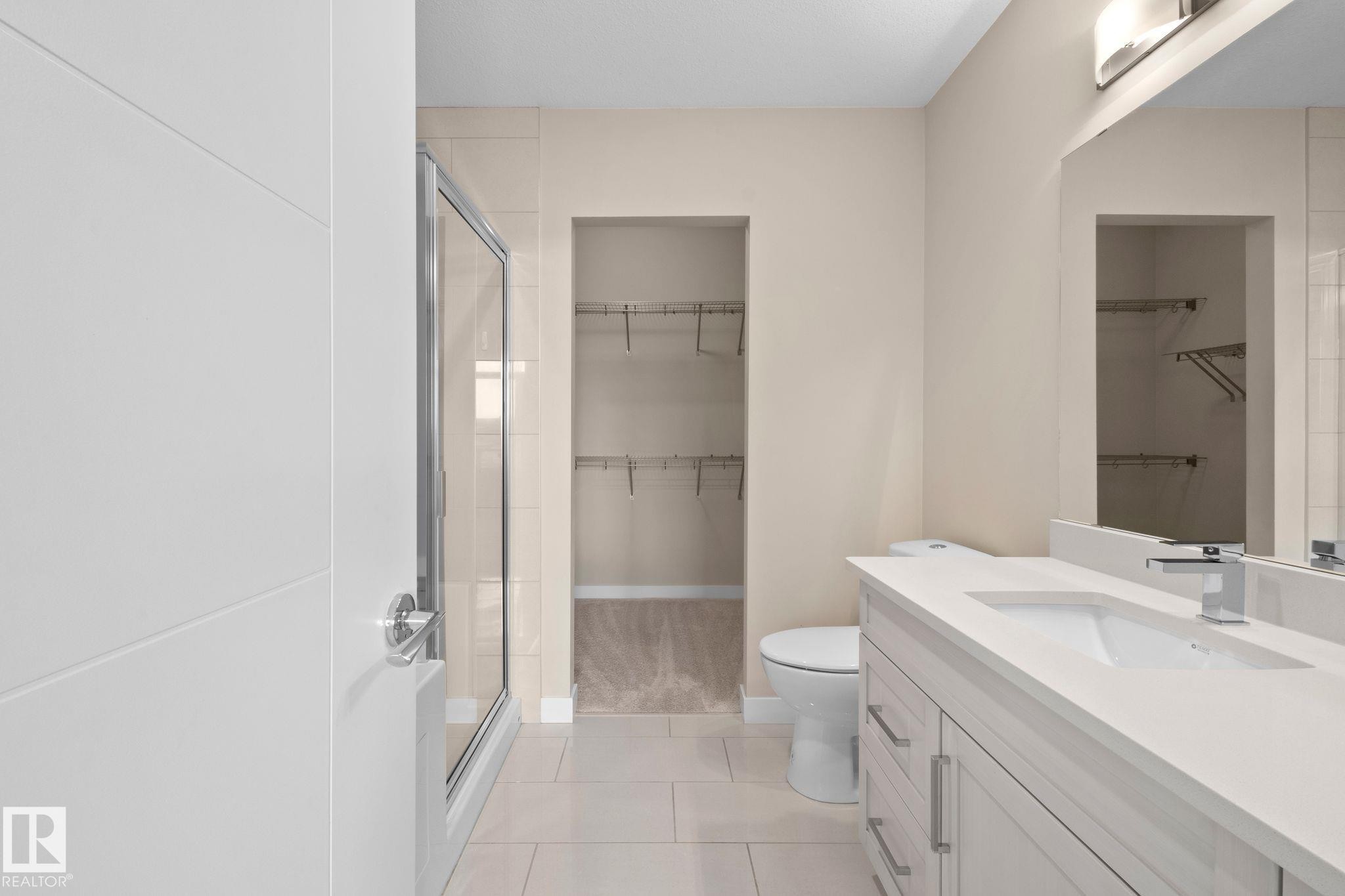 Contemporary bathroom featuring a single vanity with a white countertop and undermount sink, a framed mirror, and a glass-enclosed shower - 309 625 Leger Way, Edmonton, AB