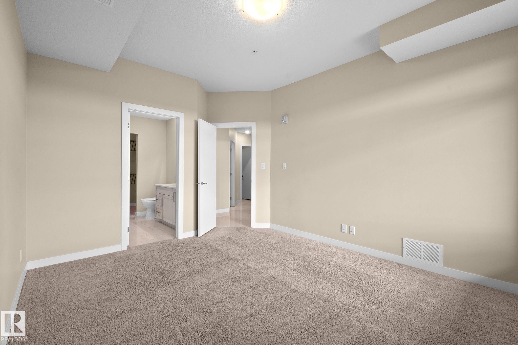 Neutral-toned carpet flooring and light beige walls create an expansive interior space - 309 625 Leger Way, Edmonton, AB