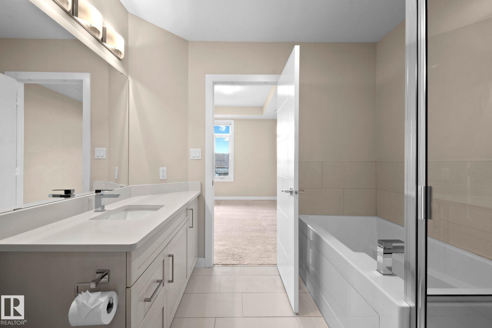 Contemporary bathroom featuring a long vanity with an integrated sink, polished chrome faucet, and under-cabinet storage - 309 625 Leger Way, Edmonton, AB