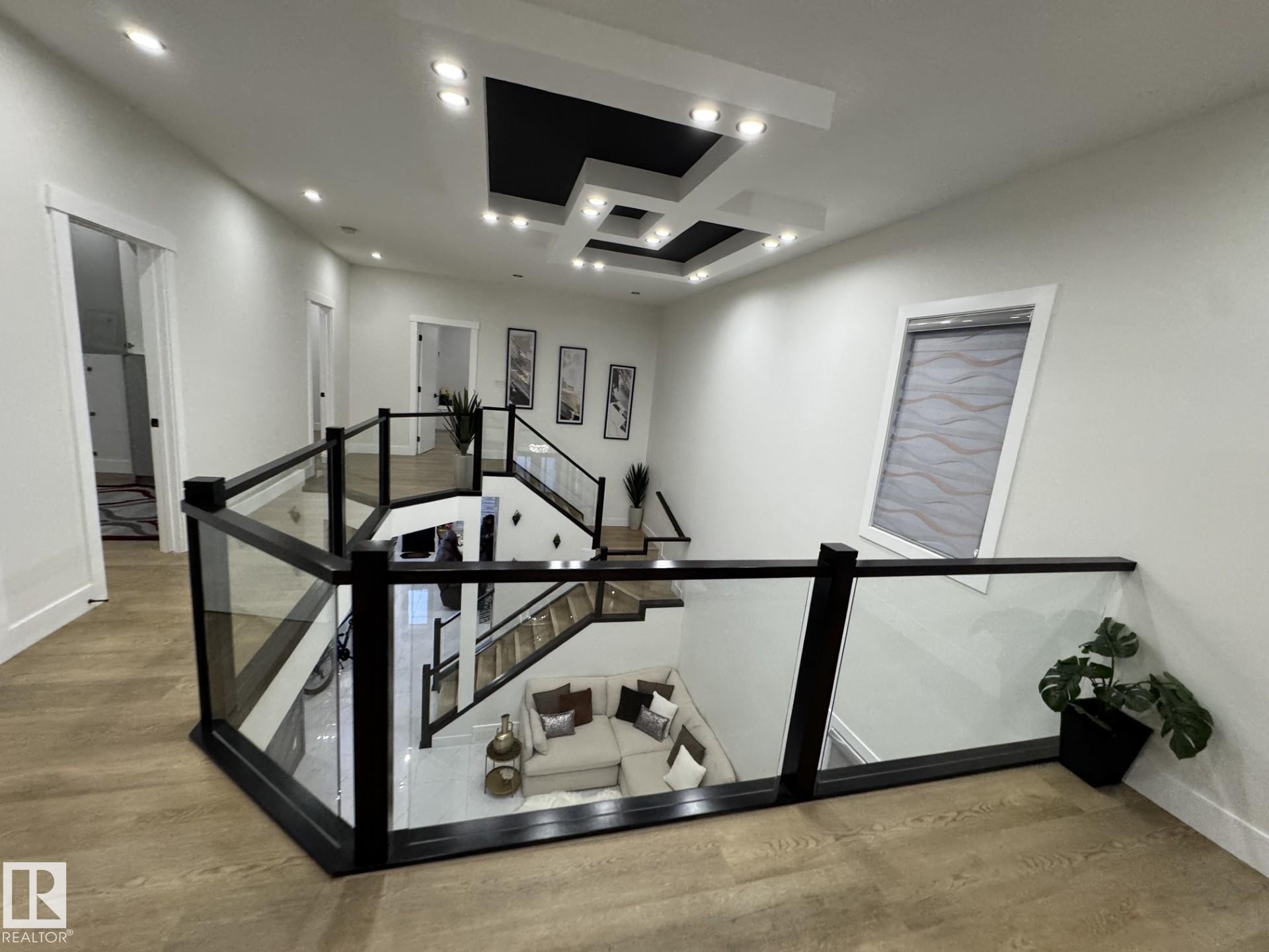 Upper-level landing featuring wood-finish flooring, a contemporary glass and black railing system, a tray ceiling with recessed lighting, and a sloped window - 2123 18 Avenue, Edmonton, AB
