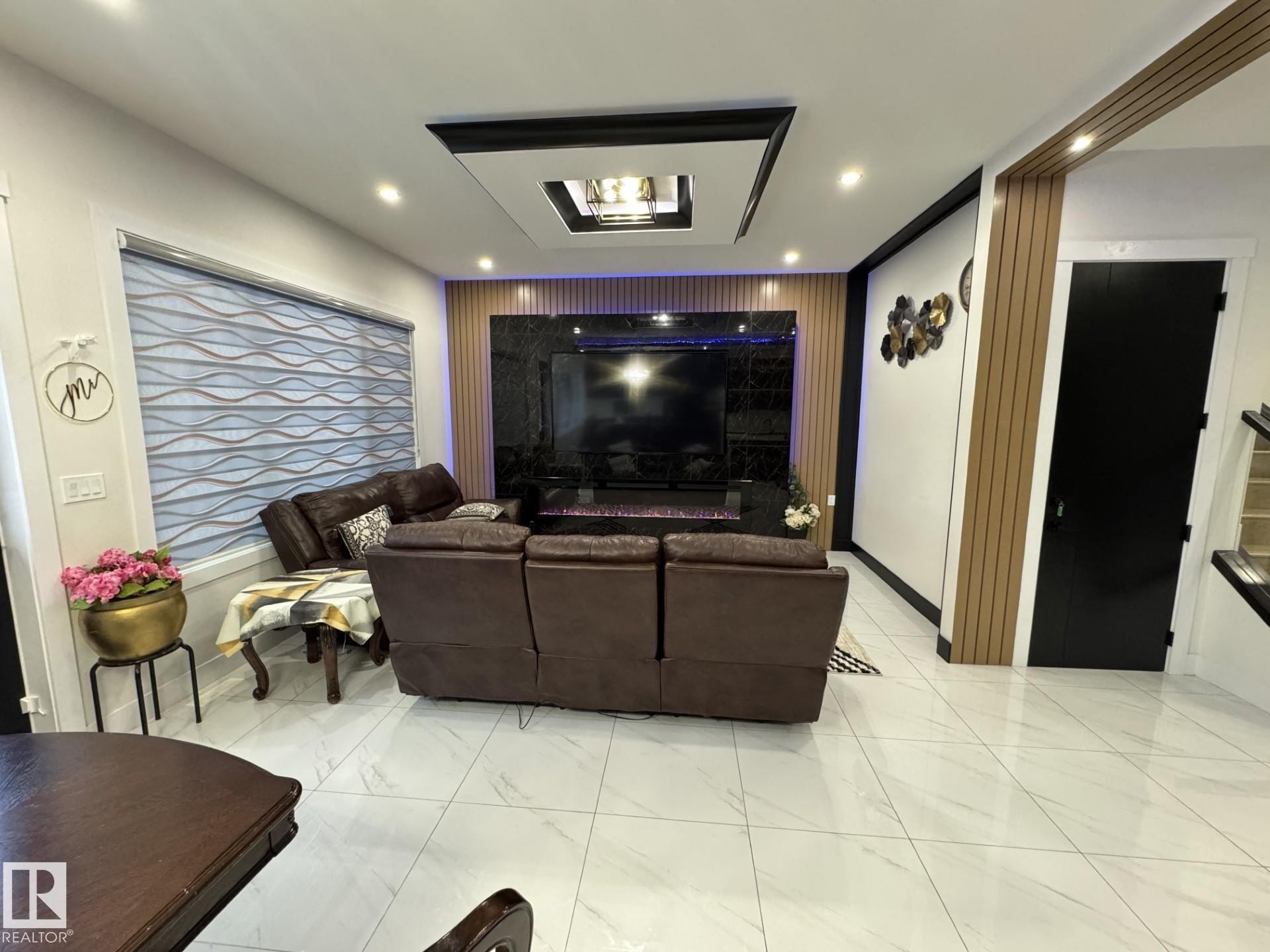Living area featuring a dark marble-finish media wall with built-in fireplace, a rectangular coffered ceiling with recessed lighting, and light wood-tone slat wall accents - 2123 18 Avenue, Edmonton, AB