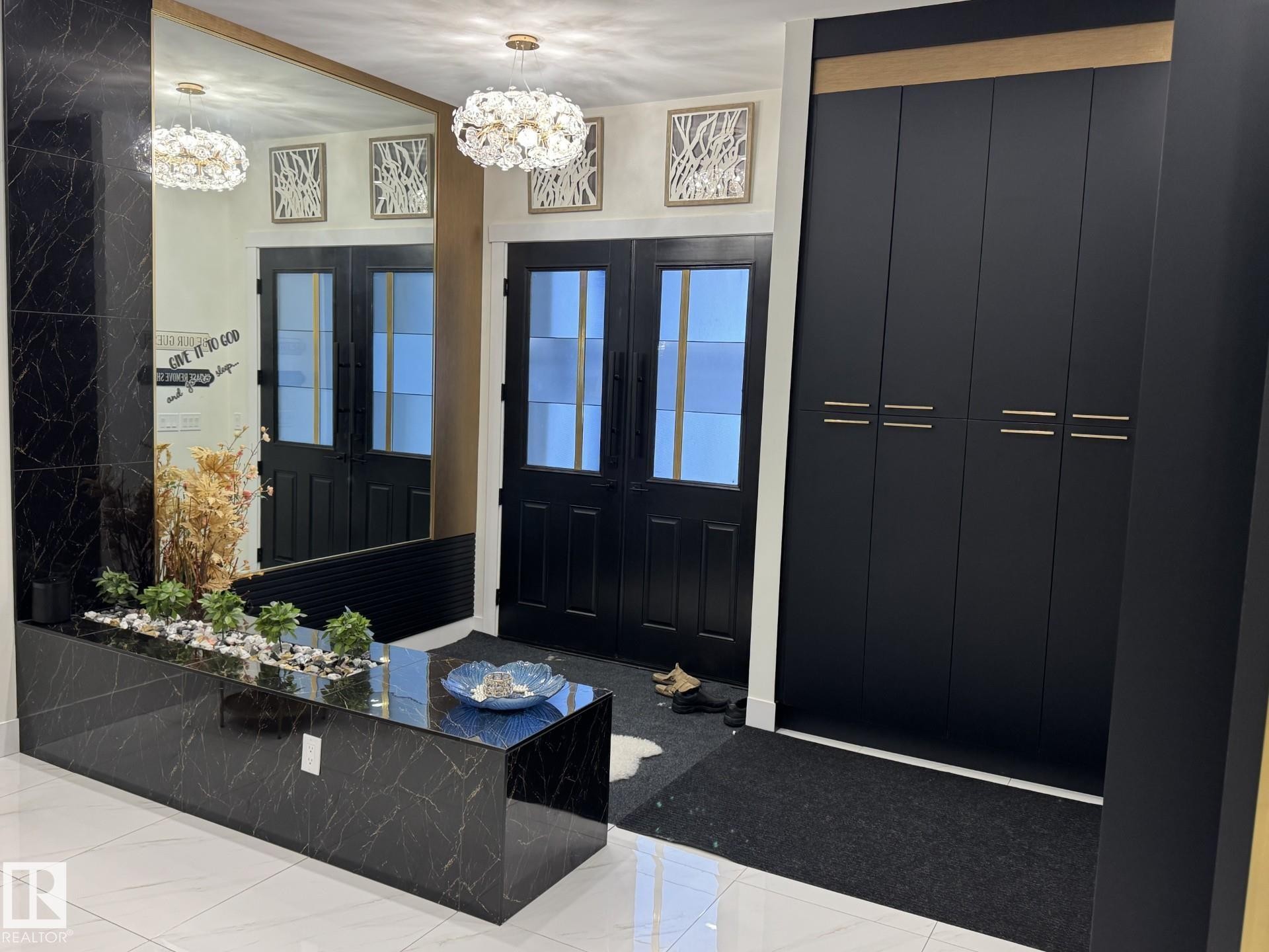 Entryway featuring a black double door, contemporary gold-tone light fixtures, built-in black cabinetry with gold-tone hardware, a large wall-mounted mirror, and a black marble-finish planter - 2123 18 Avenue, Edmonton, AB