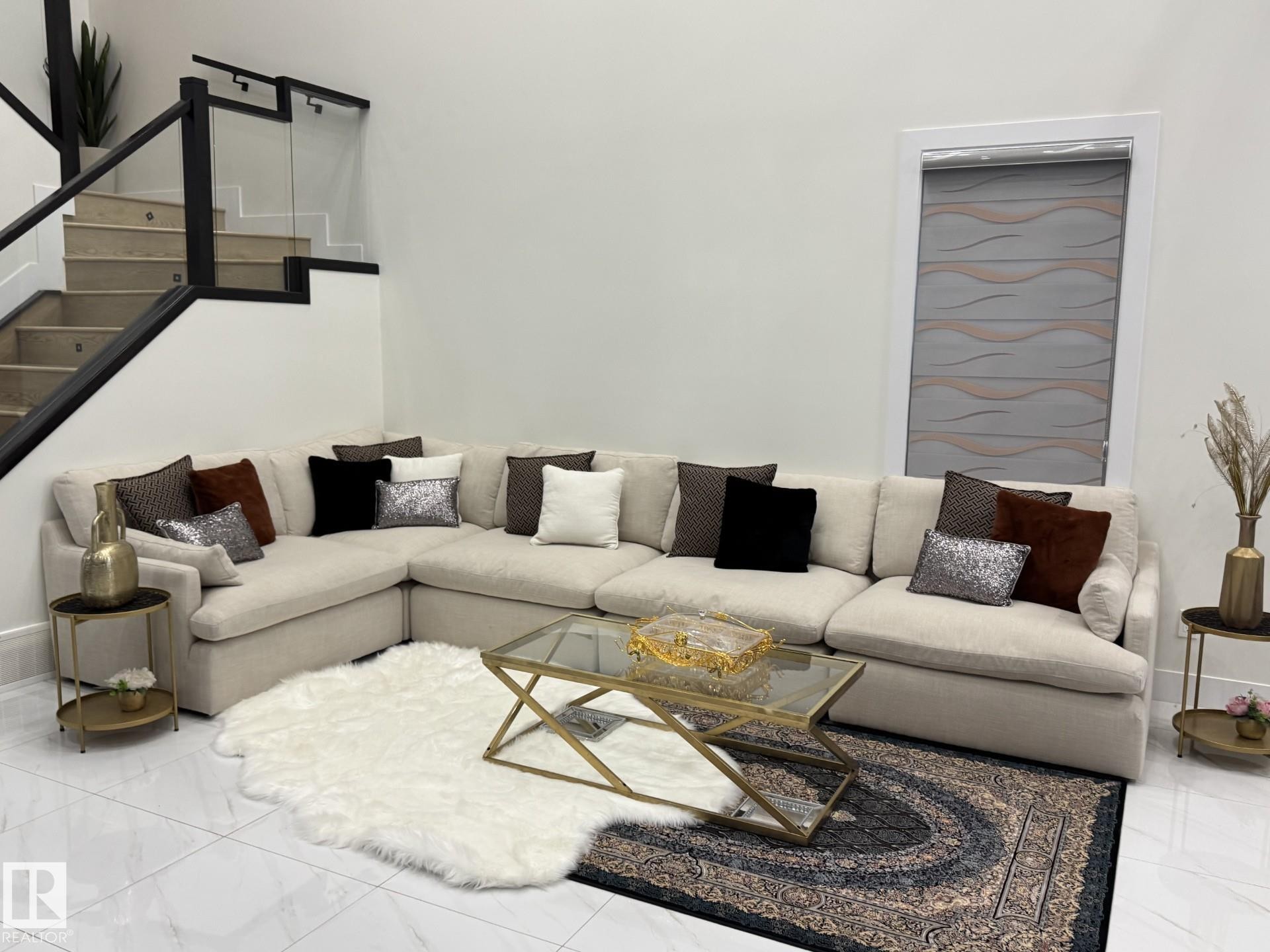 Spacious living area featuring polished tile flooring, a contemporary staircase with glass panel railing and dark wood-finish newel posts, and a window with a patterned roller shade - 2123 18 Avenue, Edmonton, AB