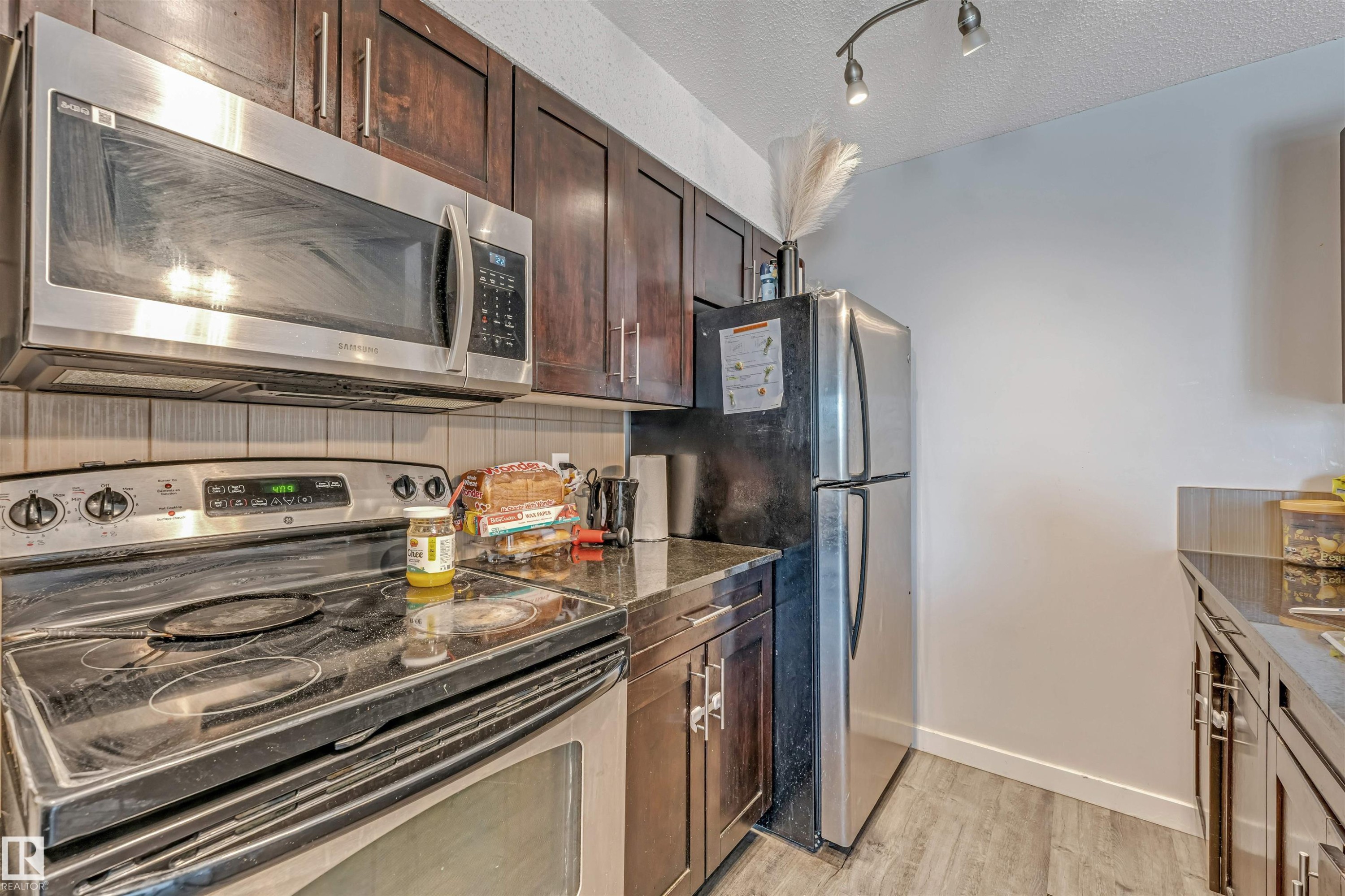 Kitchen featuring rich wood-finish cabinetry, stainless steel appliances, dark countertops, and a tiled backsplash - 320 534 Watt Boulevard, Edmonton, AB - Indoor Photo Showing Kitchen