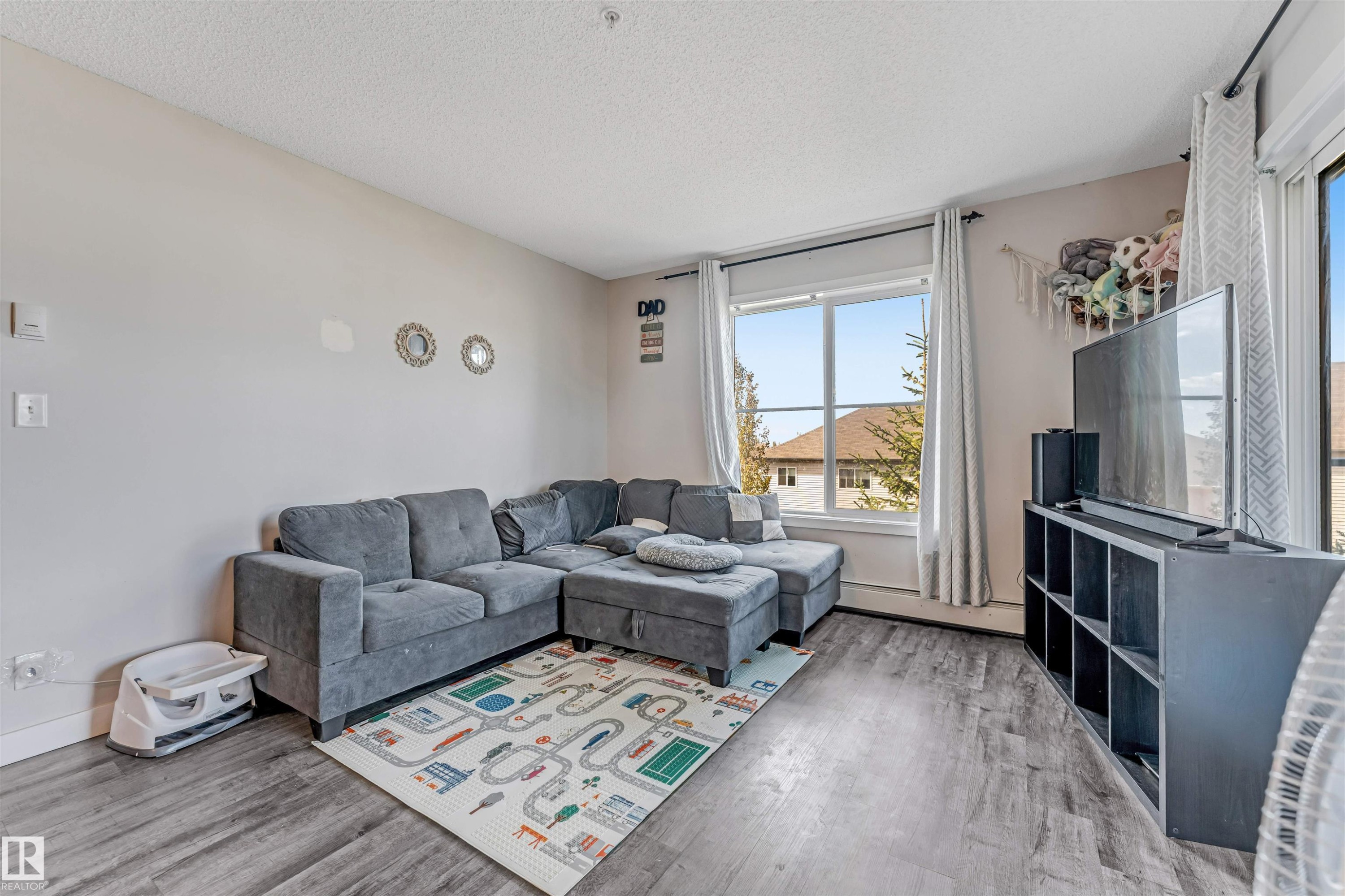 Living area featuring wood-finish flooring, light neutral wall tones, a large window, and a sliding glass door - 320 534 Watt Boulevard, Edmonton, AB - Indoor Photo Showing Living Room
