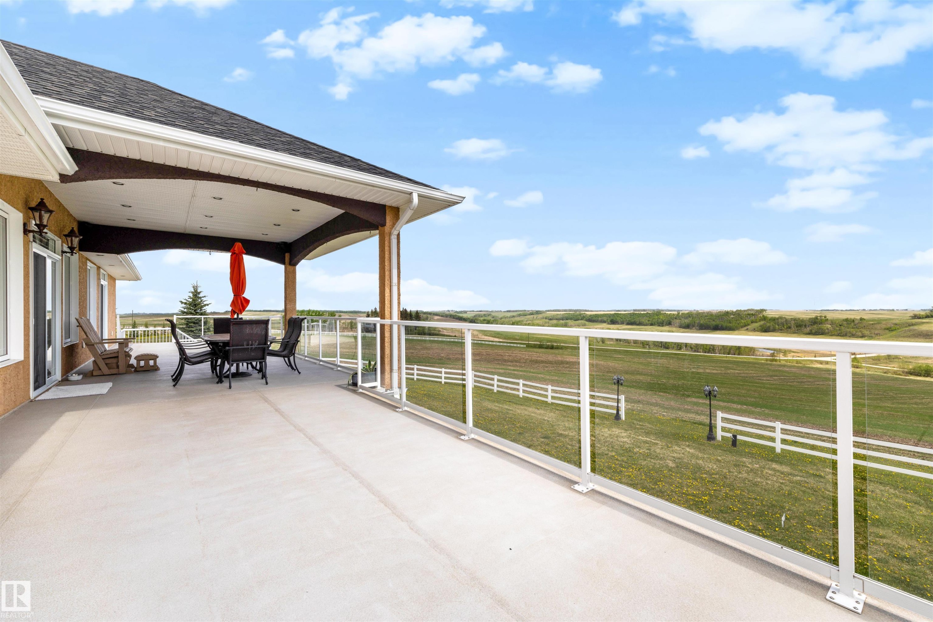 Expansive outdoor deck featuring a covered patio area with recessed lighting, an arched ceiling, and a clear glass railing system - 28125 Highway 587, Rural Red Deer County, AB - Outdoor With Deck Patio Veranda With View With Exterior