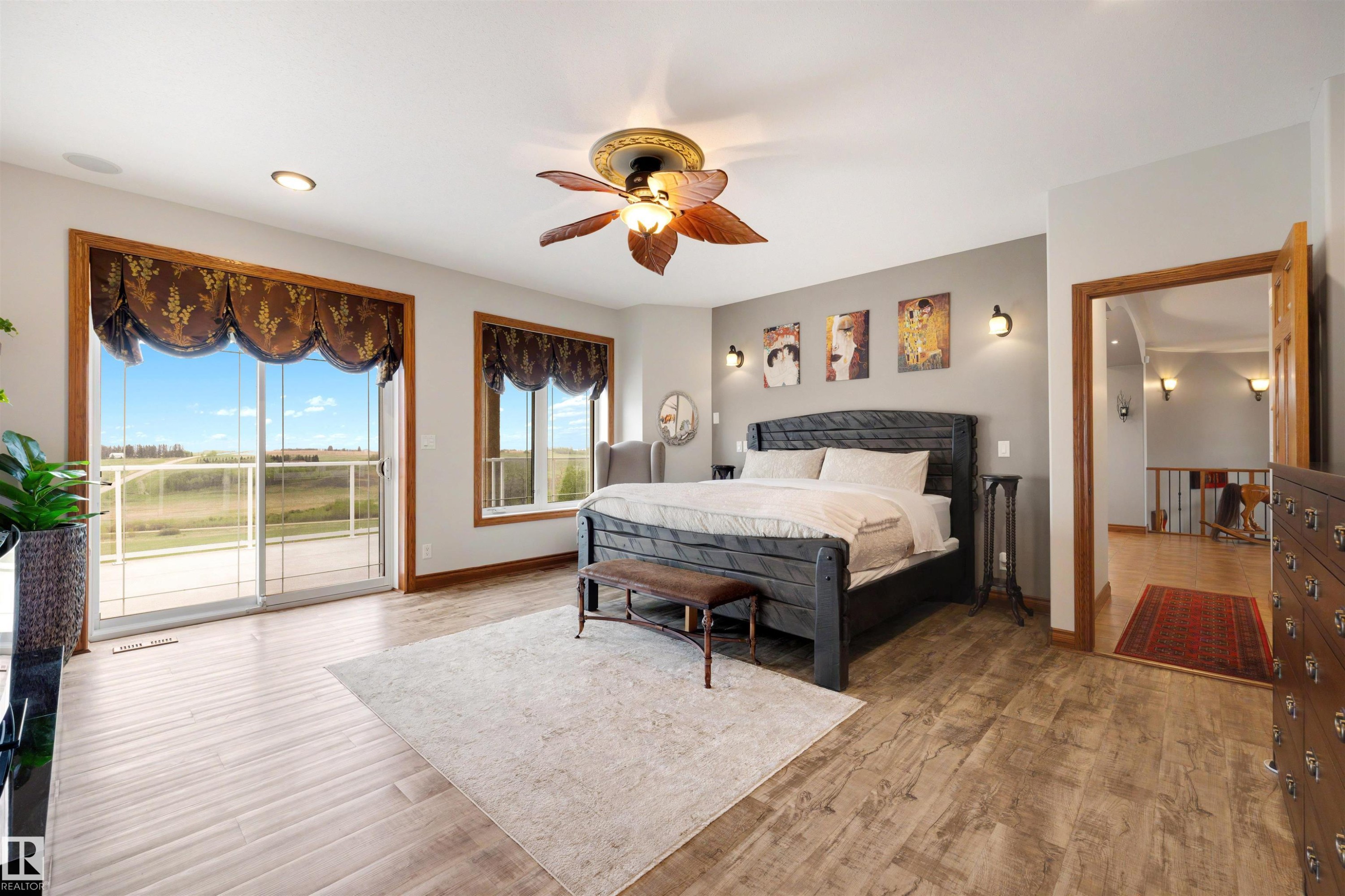 Spacious bedroom featuring wood-finish flooring, a ceiling fan with integrated lighting, and multiple windows - 28125 Highway 587, Rural Red Deer County, AB - Indoor Photo Showing Bedroom