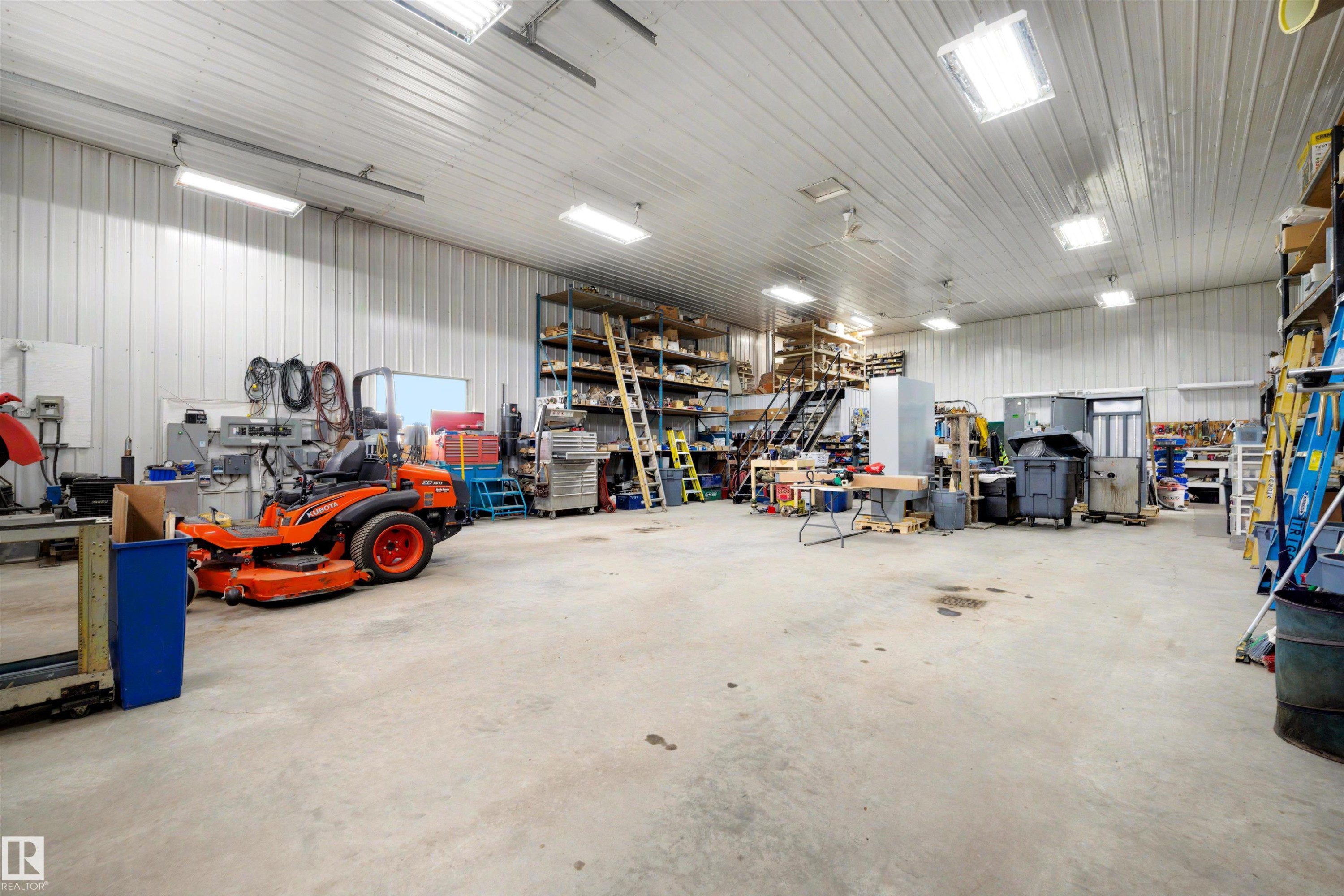 Spacious utility building featuring a concrete floor, high ceilings with fluorescent lighting, and extensive built-in shelving for storage - 28125 Highway 587, Rural Red Deer County, AB - Indoor Photo Showing Garage