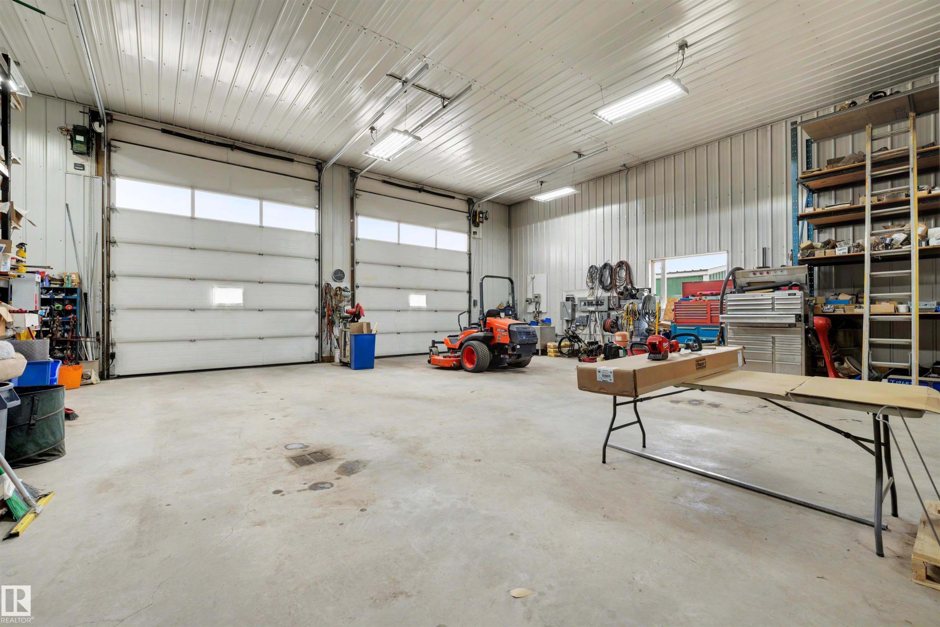 Spacious garage featuring two overhead doors with translucent panels, concrete flooring, corrugated metal walls, and overhead fluorescent lighting - 28125 Highway 587, Rural Red Deer County, AB - Indoor Photo Showing Garage