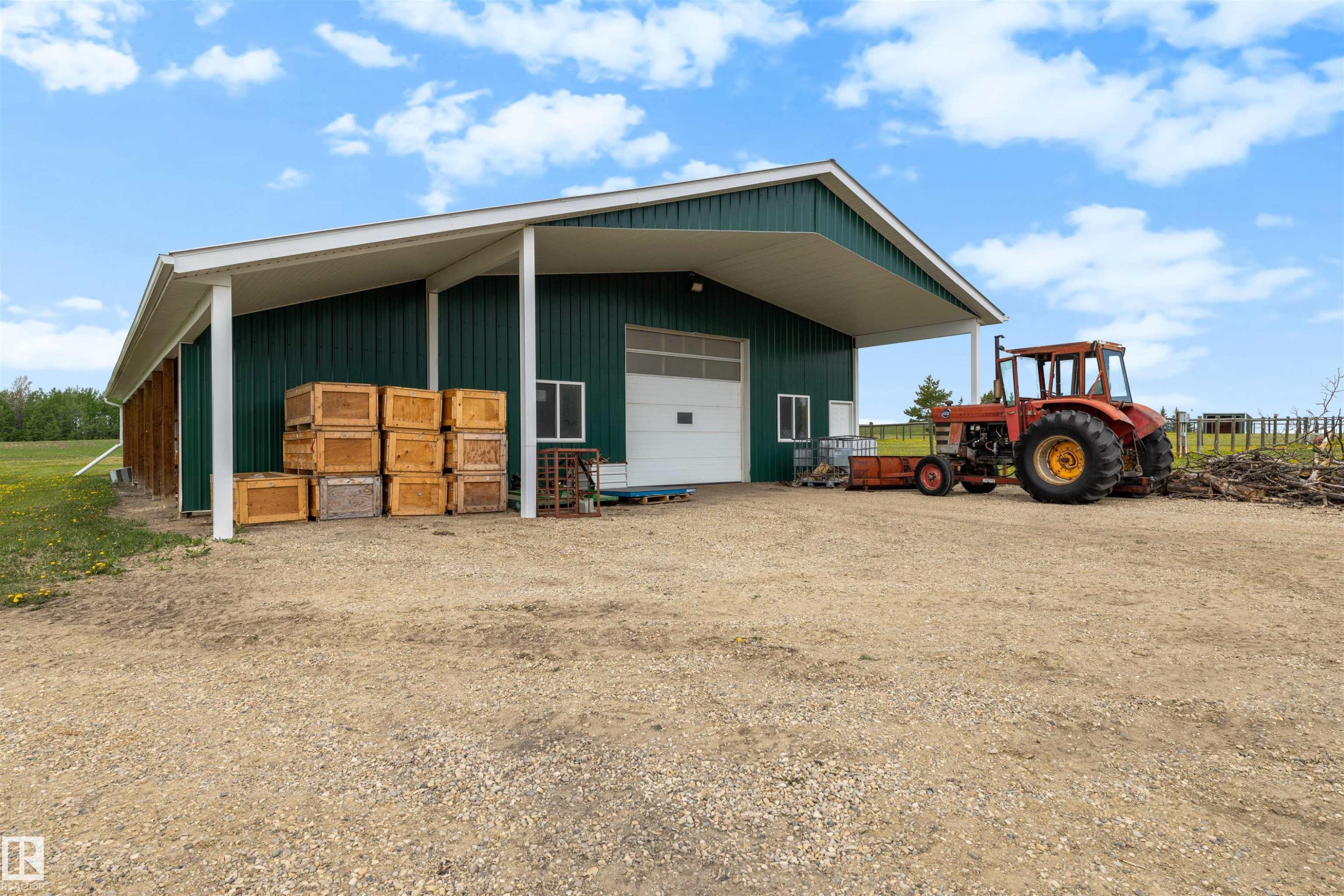 Green metal building with a white overhead door, an extended white covered overhang, and a gravel foreground - 28125 Highway 587, Rural Red Deer County, AB - Outdoor