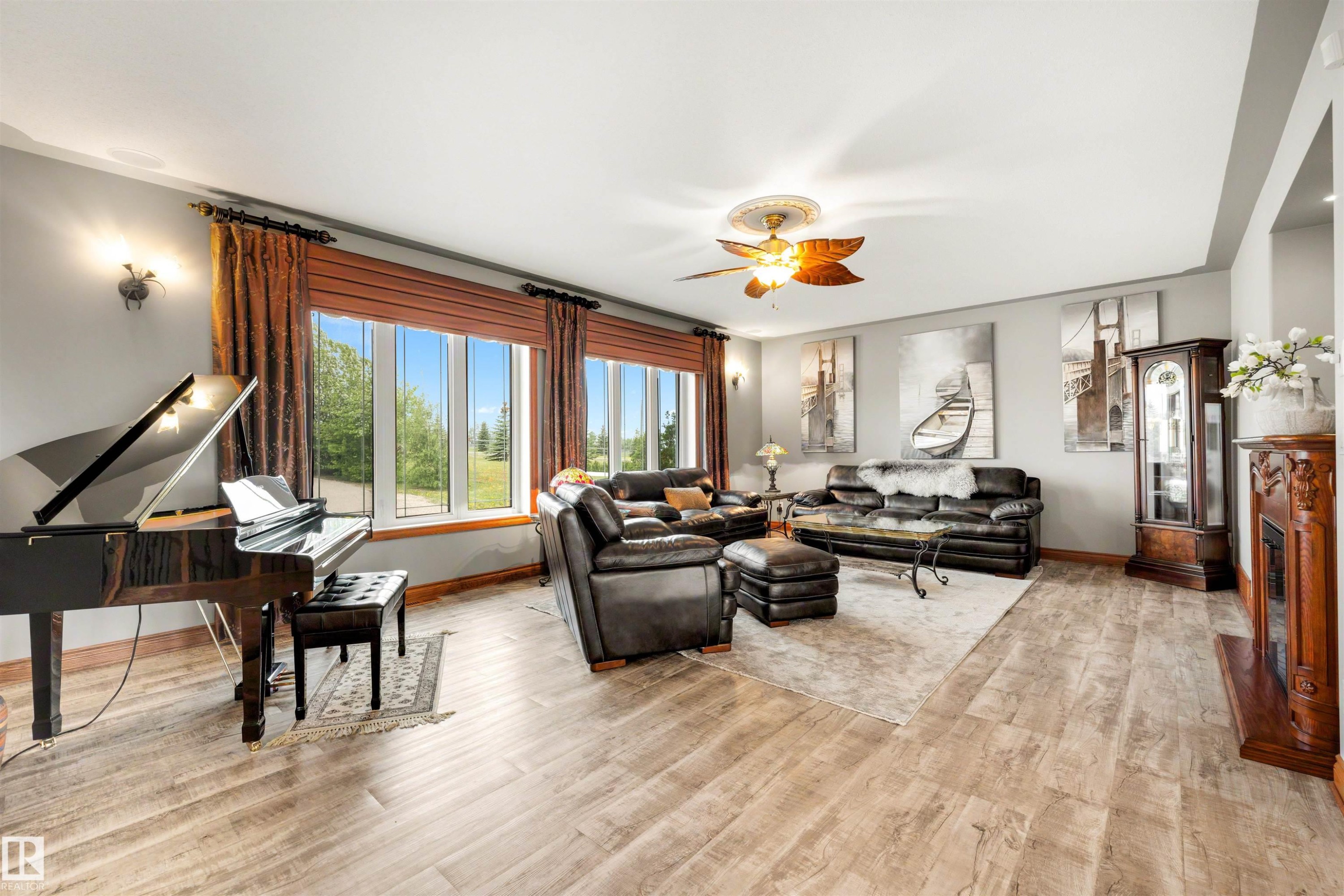 Spacious living area featuring large windows, light wood-finish flooring, a decorative ceiling fan, and a built-in fireplace with an ornate wooden mantel - 28125 Highway 587, Rural Red Deer County, AB - Indoor
