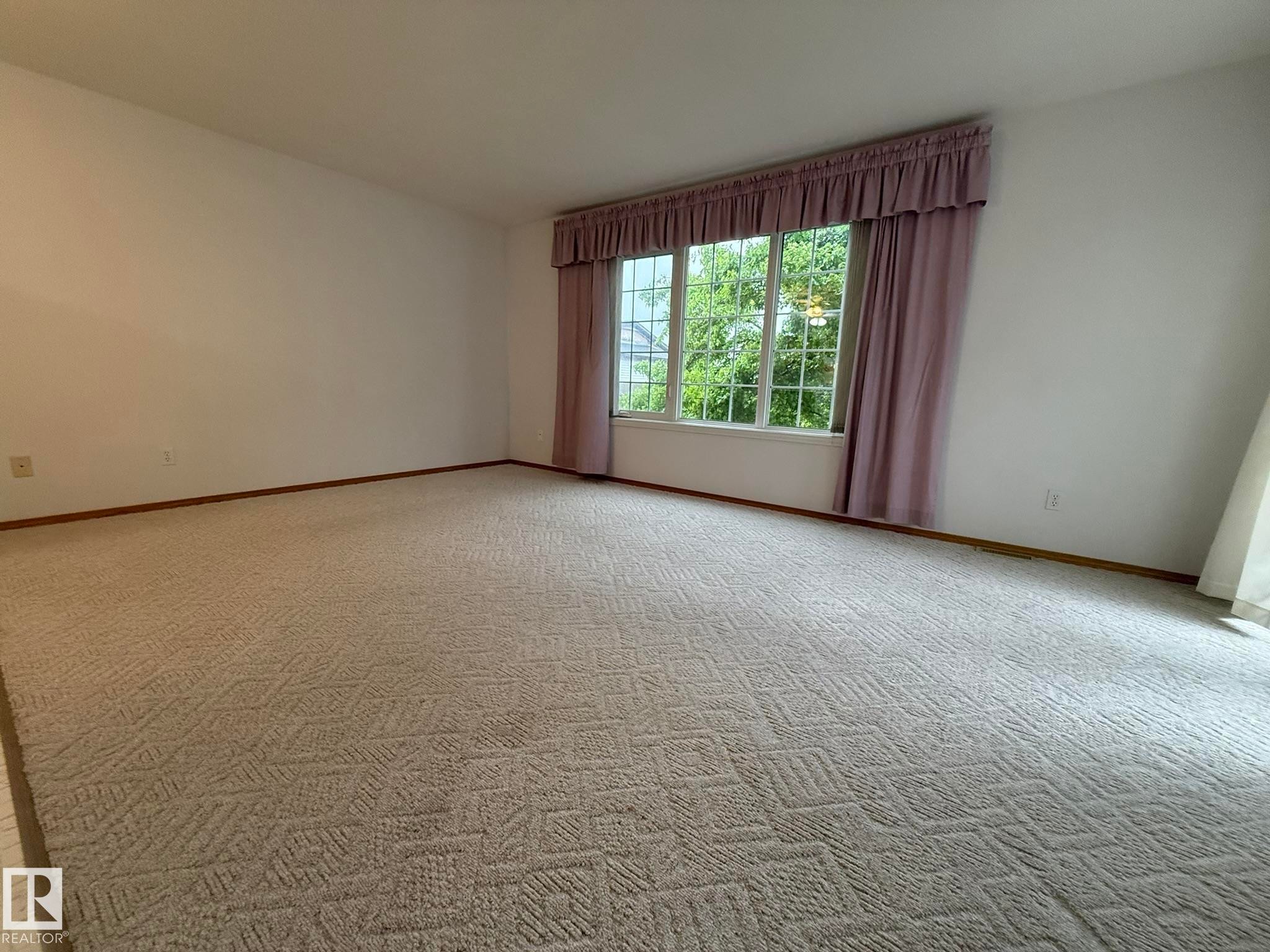 Expansive room featuring patterned carpeting, white walls, and wood-finish baseboards - 102 4610 50 Avenue, Stony Plain, AB