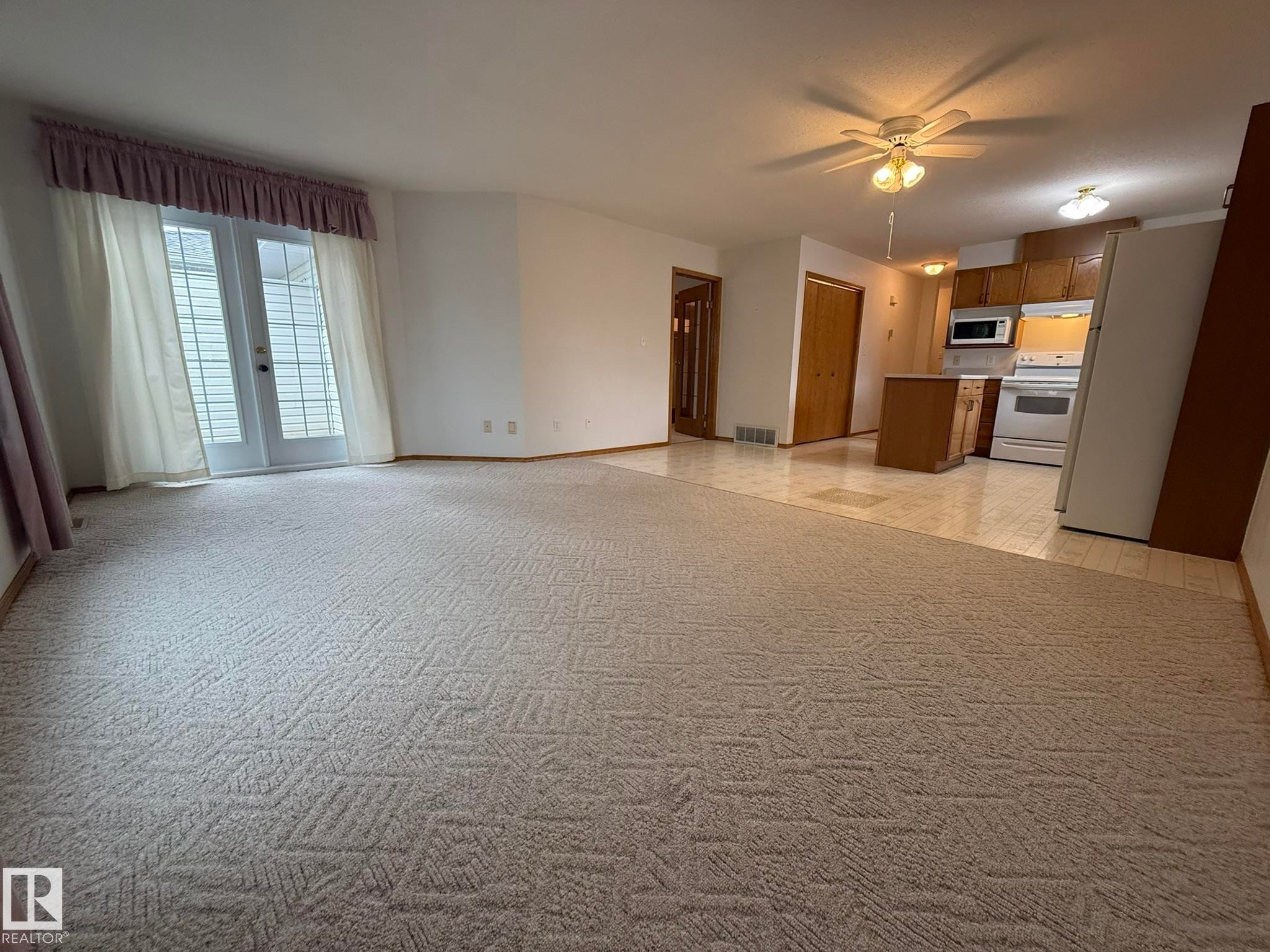 Carpeted living area featuring white double doors with horizontal blinds - 102 4610 50 Avenue, Stony Plain, AB