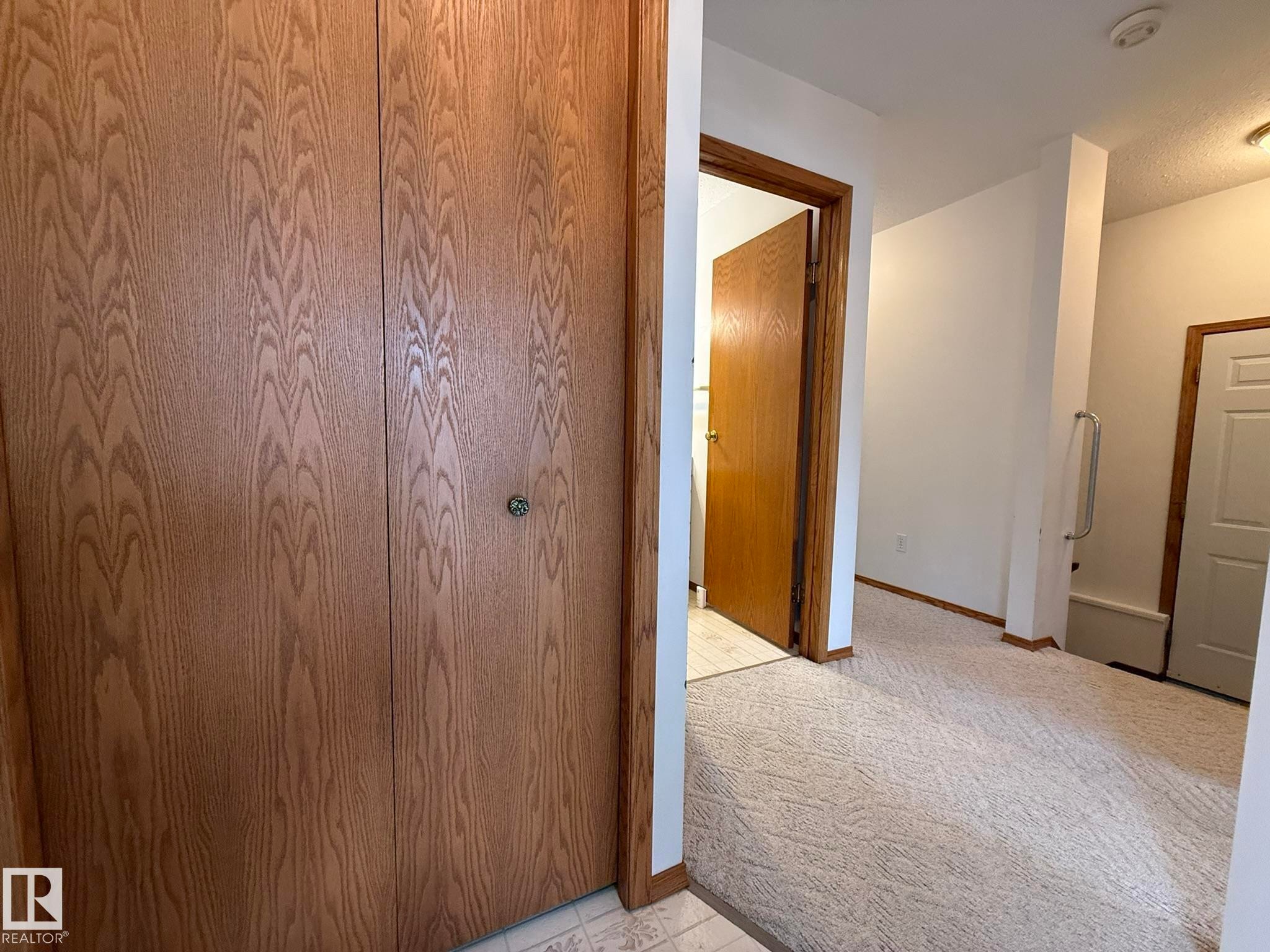 Wood-finish bi-fold closet doors with a decorative knob - 102 4610 50 Avenue, Stony Plain, AB