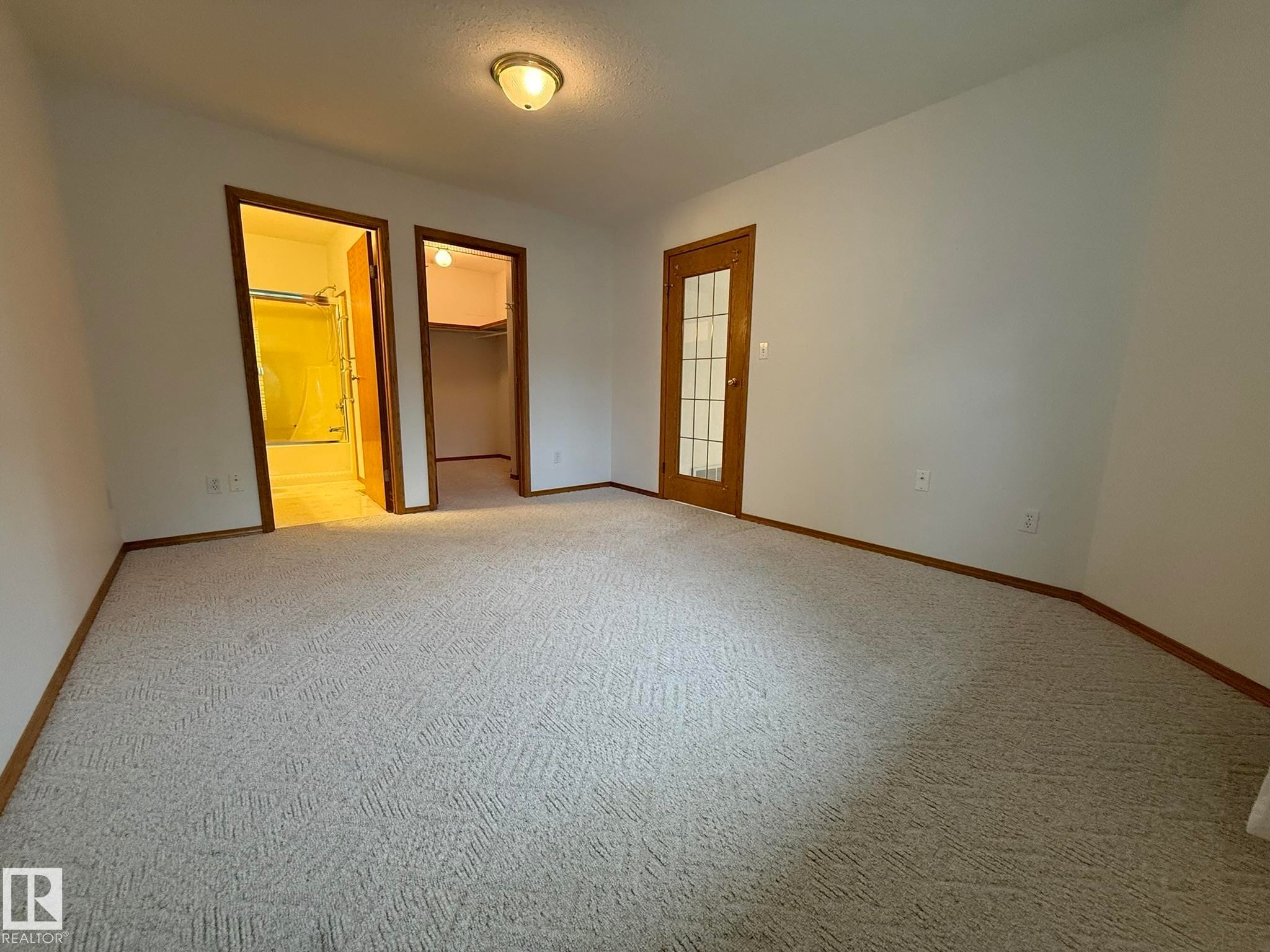 Spacious room featuring light-colored patterned carpeting, white walls, and wood trim - 102 4610 50 Avenue, Stony Plain, AB