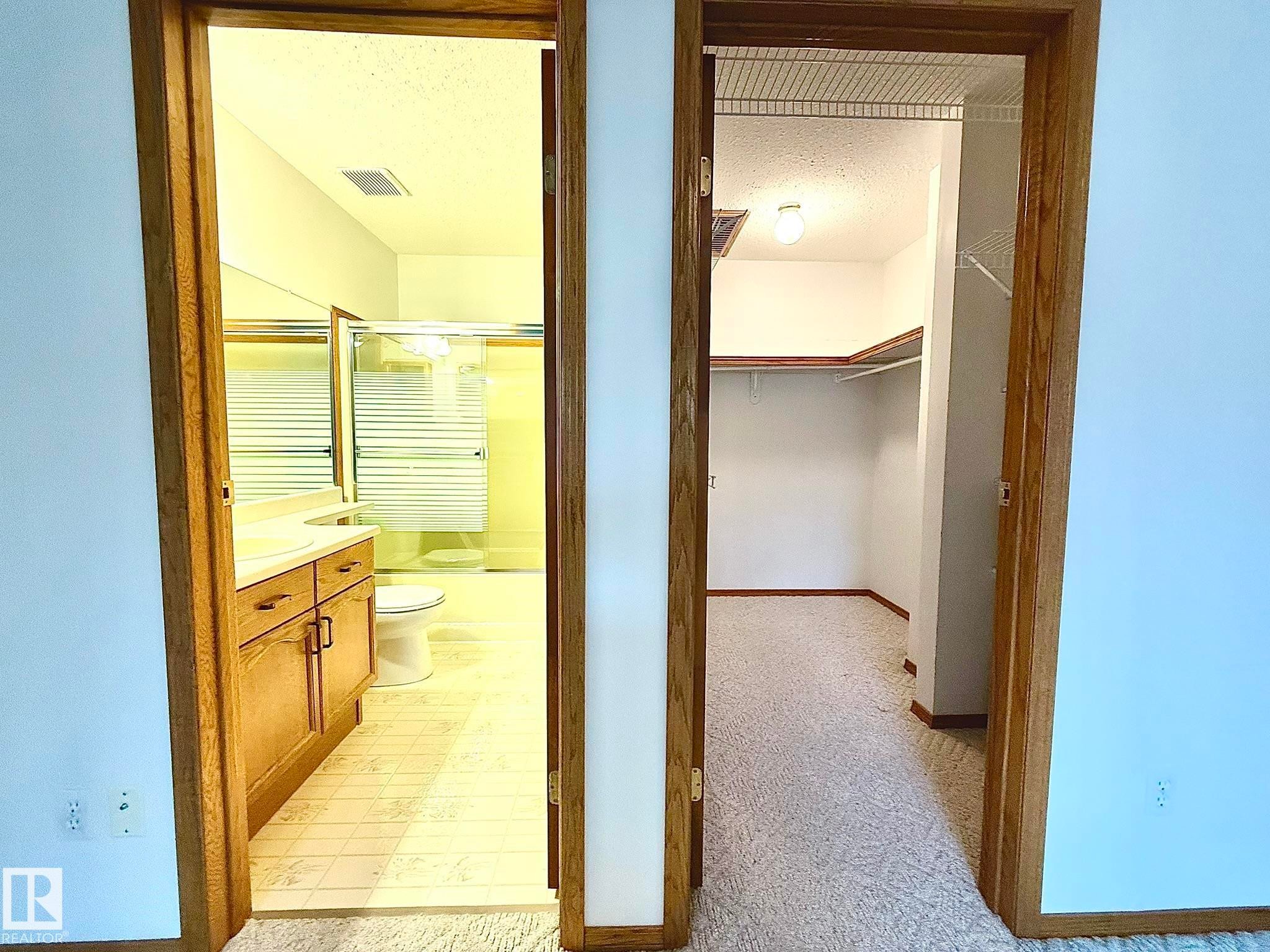 Oak-trimmed doorways opening to a full bathroom and a separate walk-in closet - 102 4610 50 Avenue, Stony Plain, AB