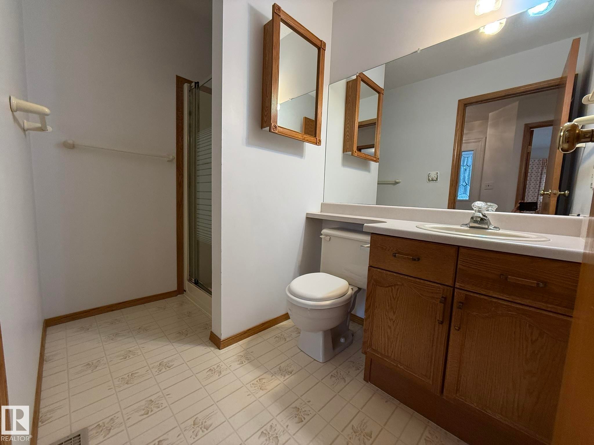 Bathroom featuring a vanity with a white countertop and wood-finish cabinetry, a built-in mirror, and a standing shower with a glass enclosure - 102 4610 50 Avenue, Stony Plain, AB