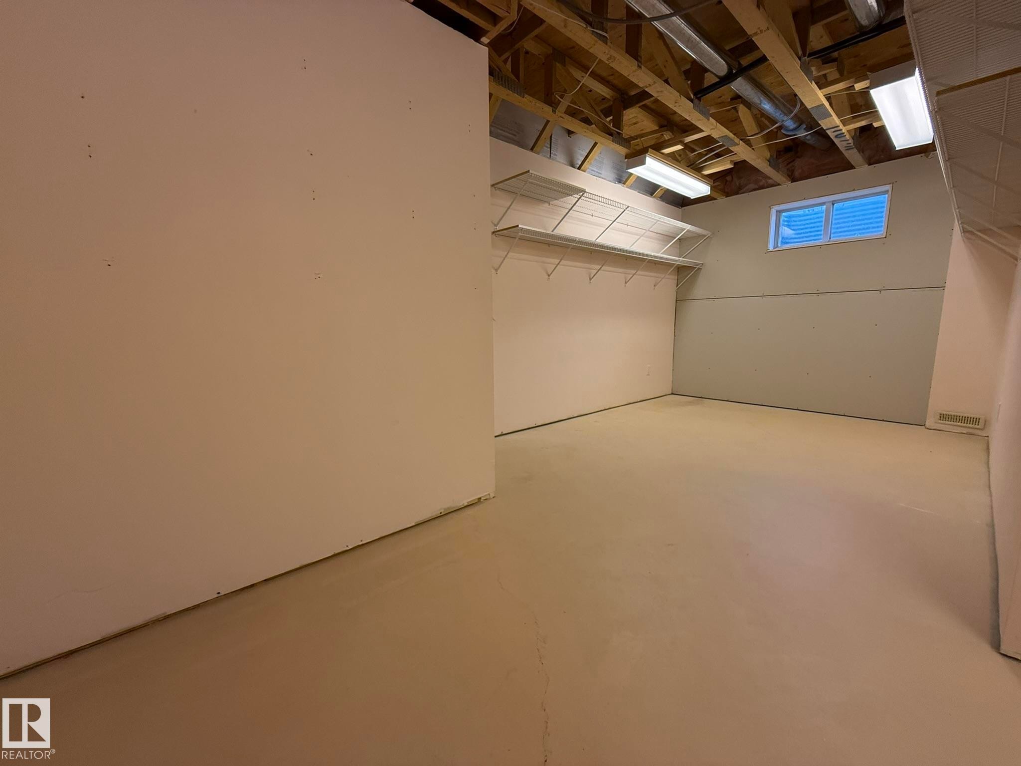 Unfinished interior space featuring exposed ceiling joists, overhead lighting, and a basement window - 102 4610 50 Avenue, Stony Plain, AB